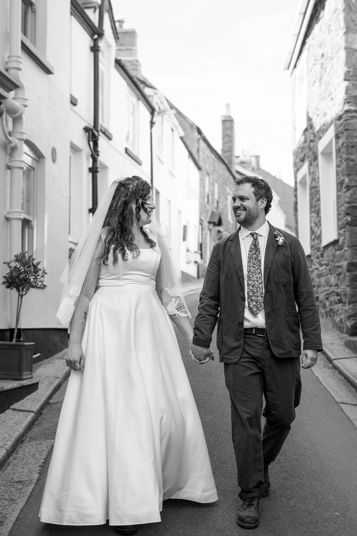 Candid photo of bride and groom walking through their Cornish village on their wedding day