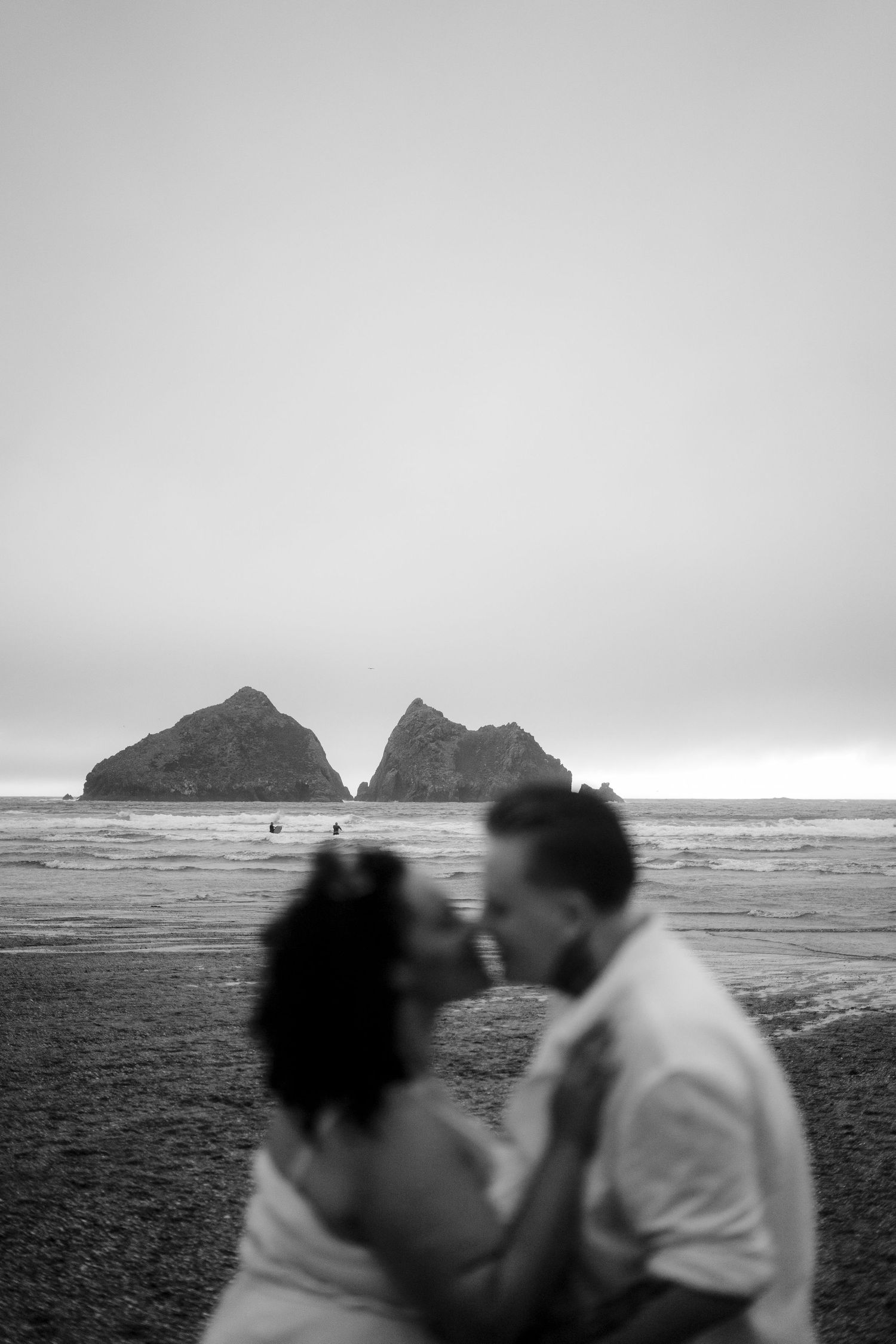 Black and white candid photo of two women kissing with the Cornish coast in the background