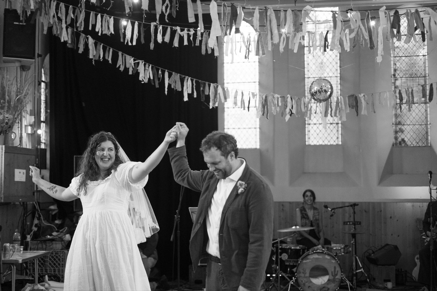 Black and white photo of bride and groom enjoying their first dance in the village hall at their garden party wedding