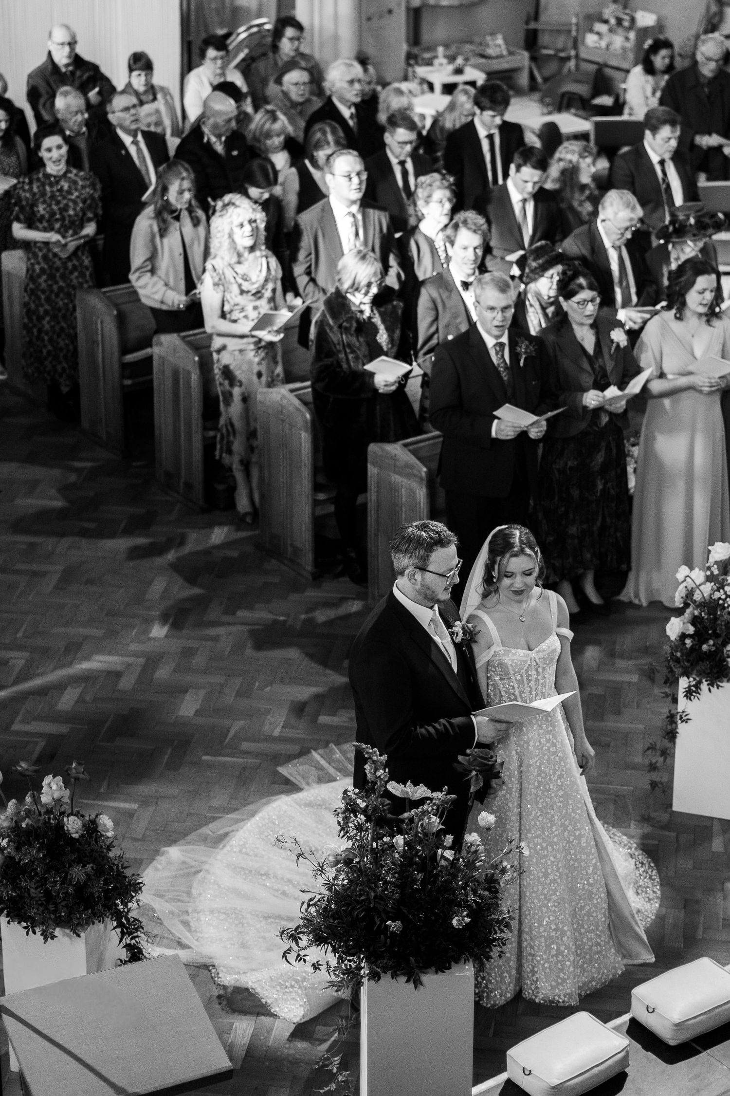 Black and white aerial view of a wedding ceremony in Penzance Church, with bride and groom standing before officiant