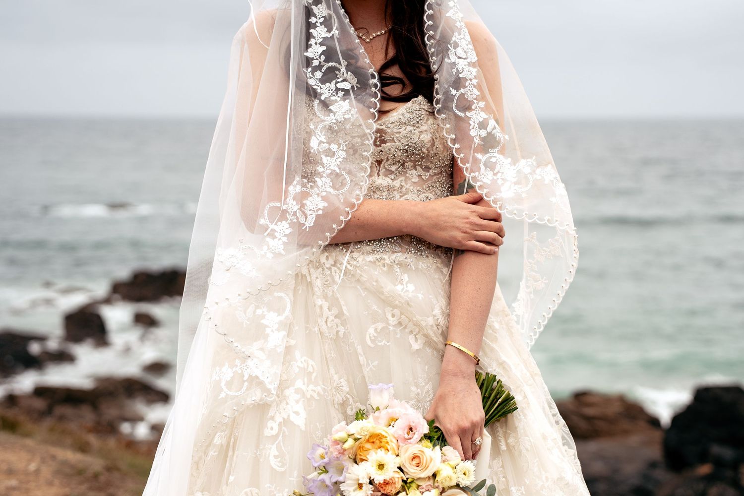 Detail photos of a bride's dress, veil and bouquet with the beautiful backdrop of the Cornish coast in St Ives, behind St Nicholas Chapel