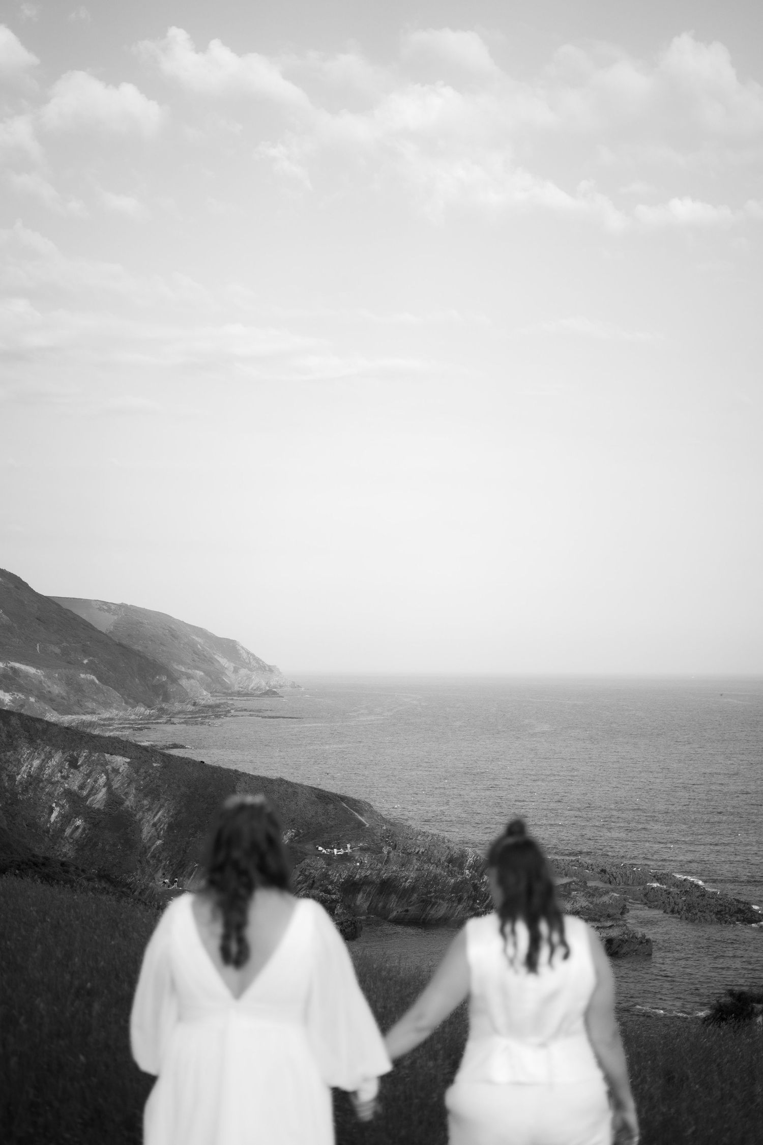 Two brides taking in the view of the Cornish coast after their wedding at Tredudwell Manor