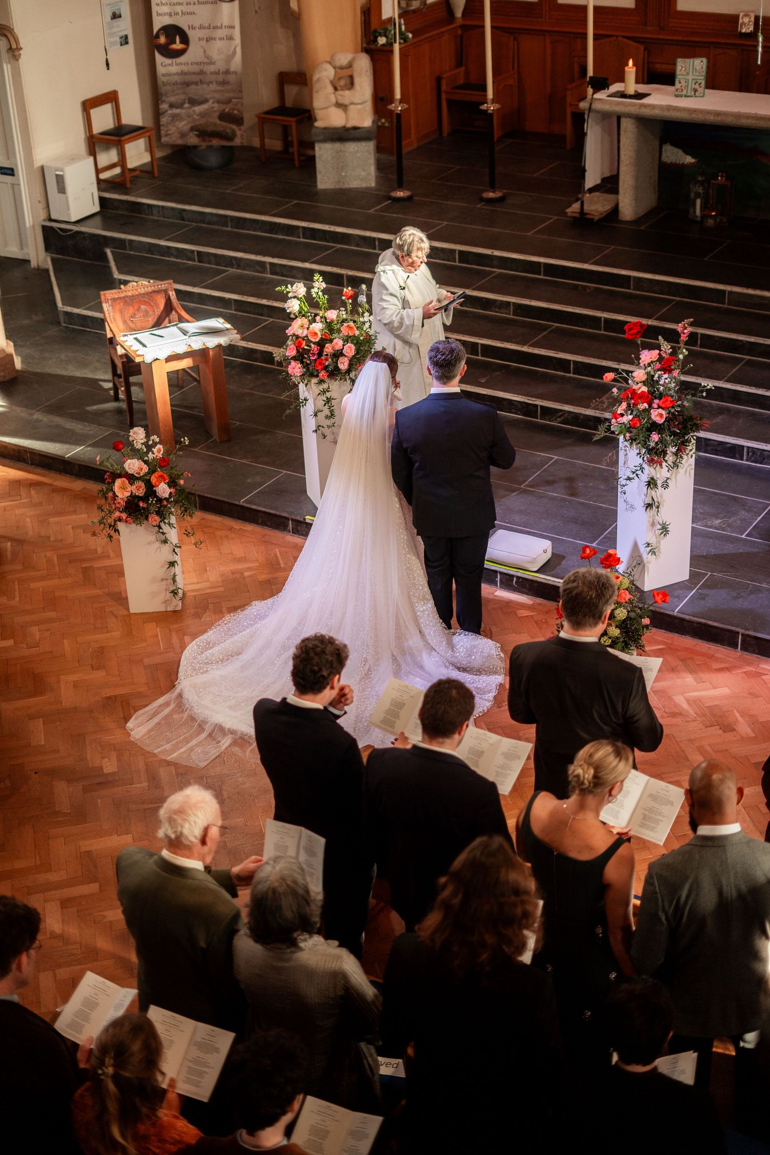 Aerial view of a wedding ceremony in a church, with bride and groom standing before officiant amid floral arrangements