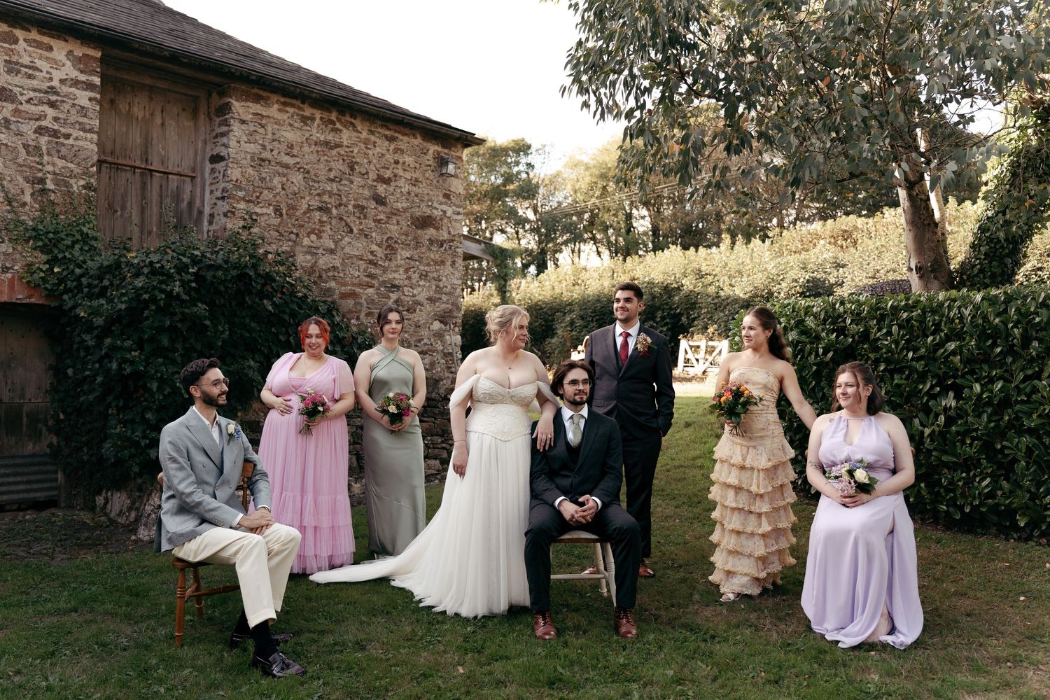 Editorial photo of bridal party, some seated and some standing, with bride and groom in the middle