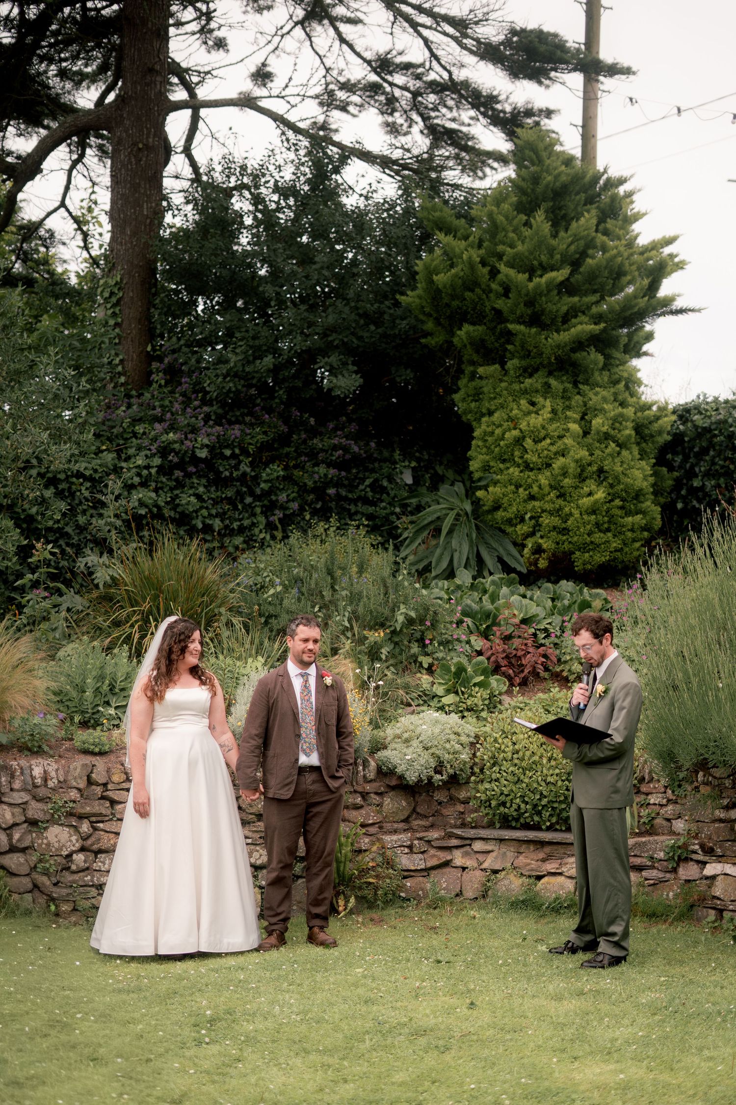 Bride and groom being married by their best friend as their celebrant, in the garden of Maker with Rame Community Hall
