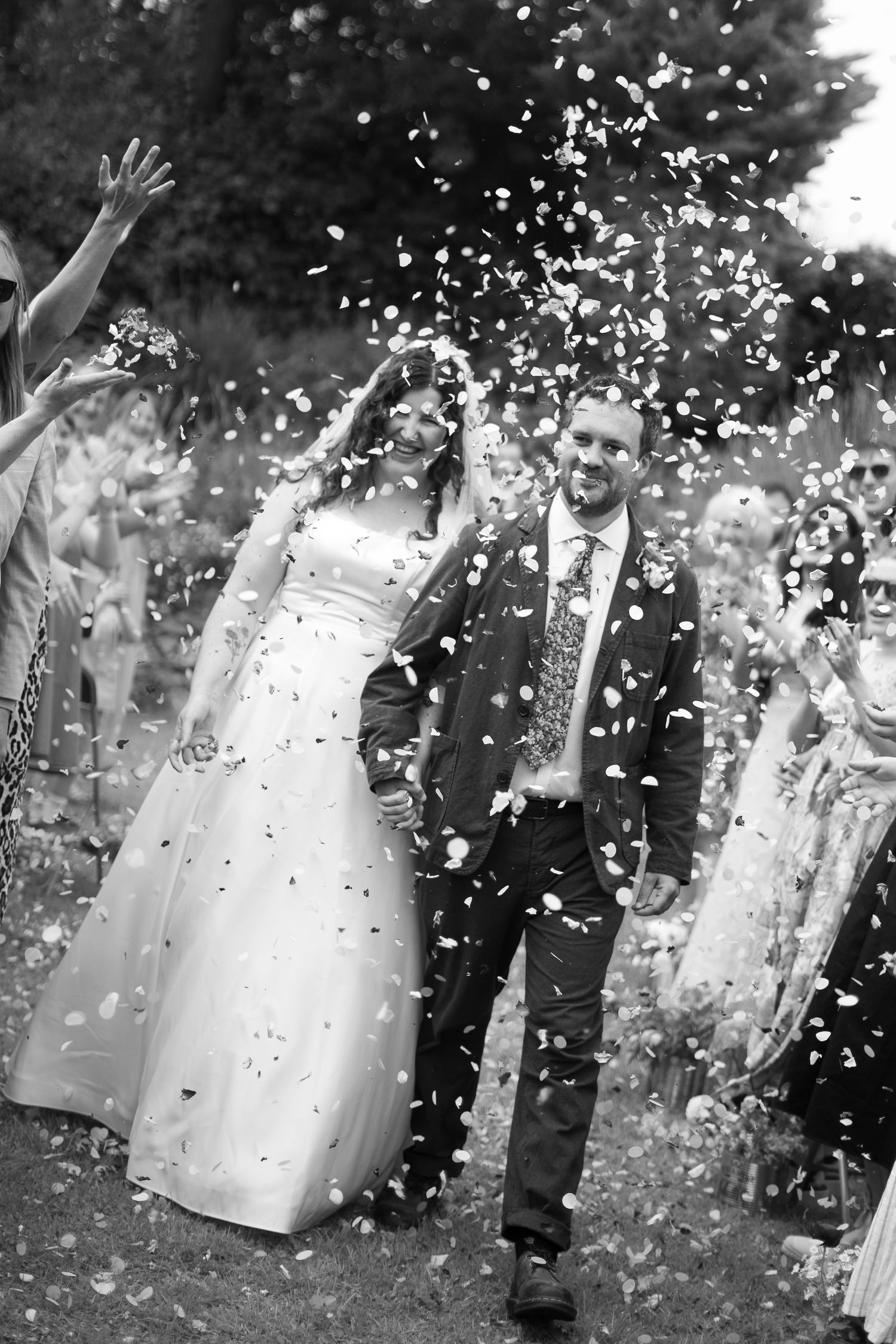 Black and white photo of bride and groom smiling through their confetti throw