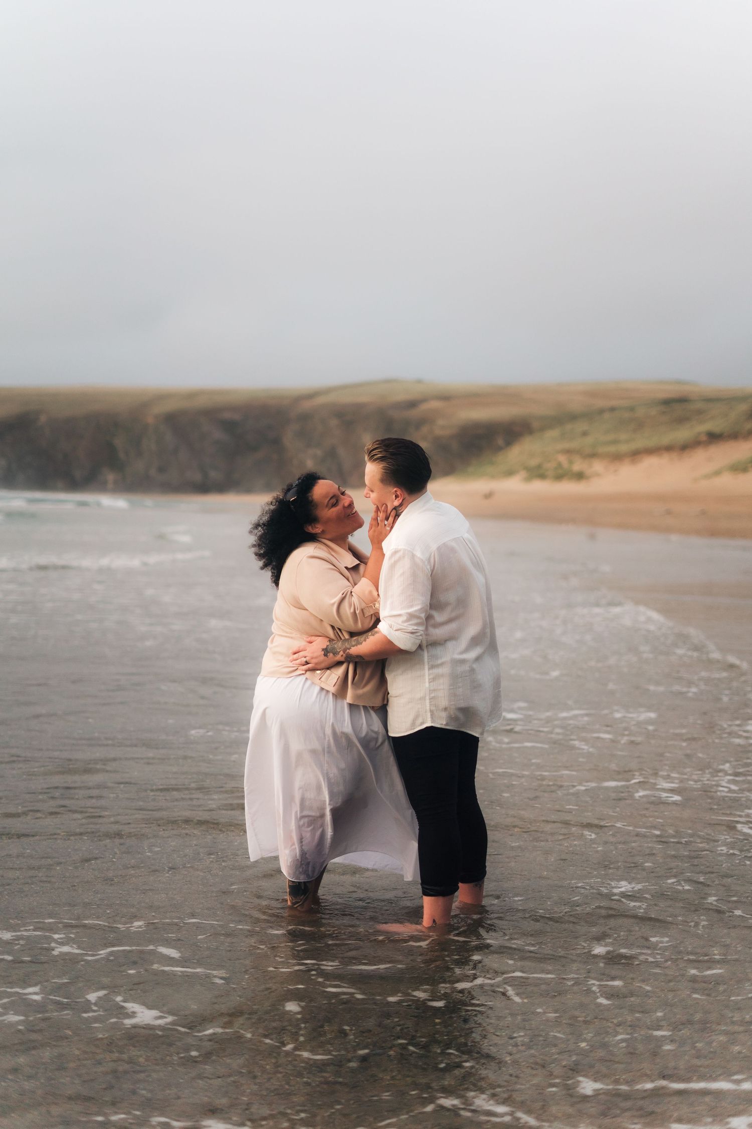 Two women standing in the Cornish sea kissing after getting engaged on the beach