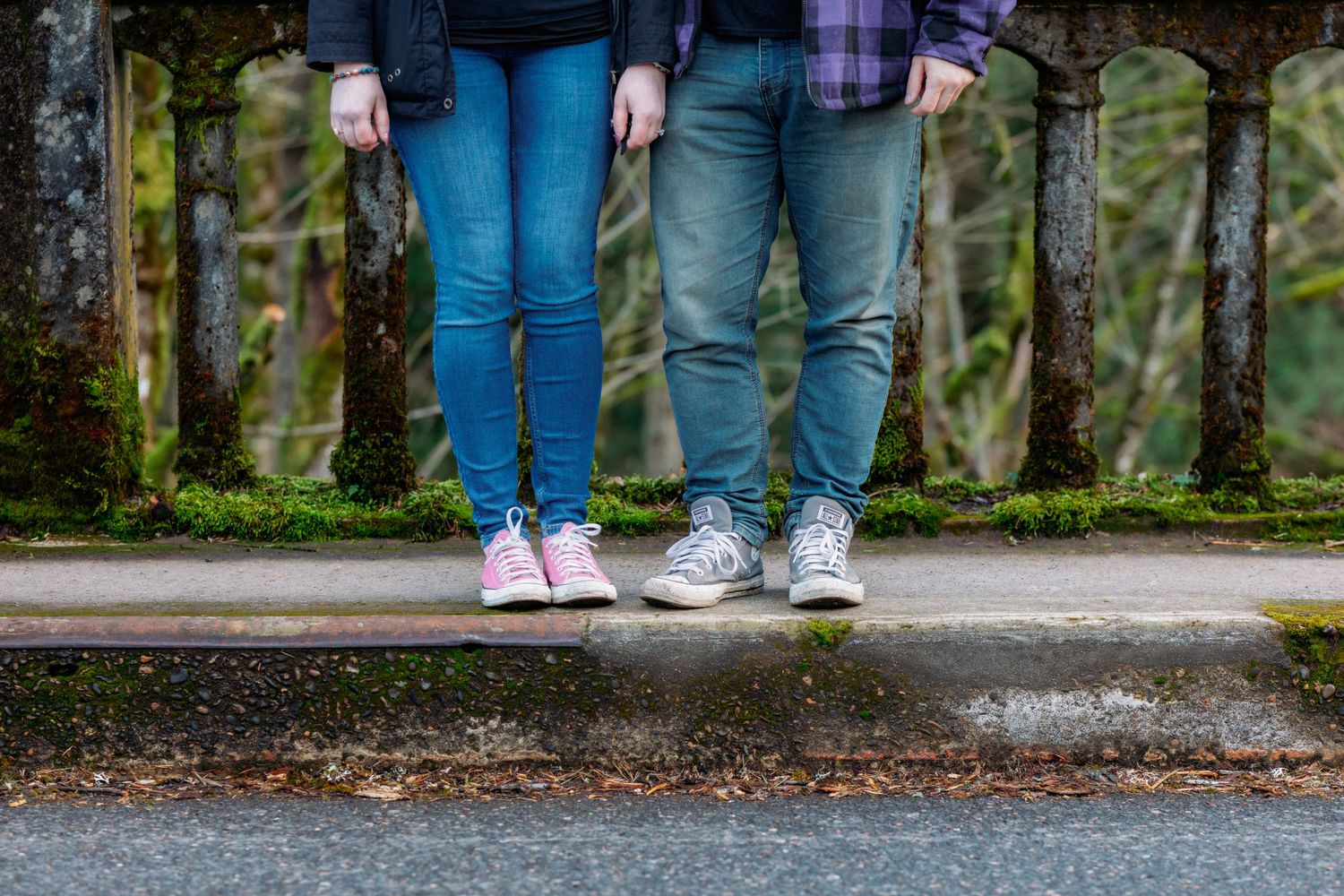 Two people in blue jeans and sneakers walk along a wet path with puddles after rain.