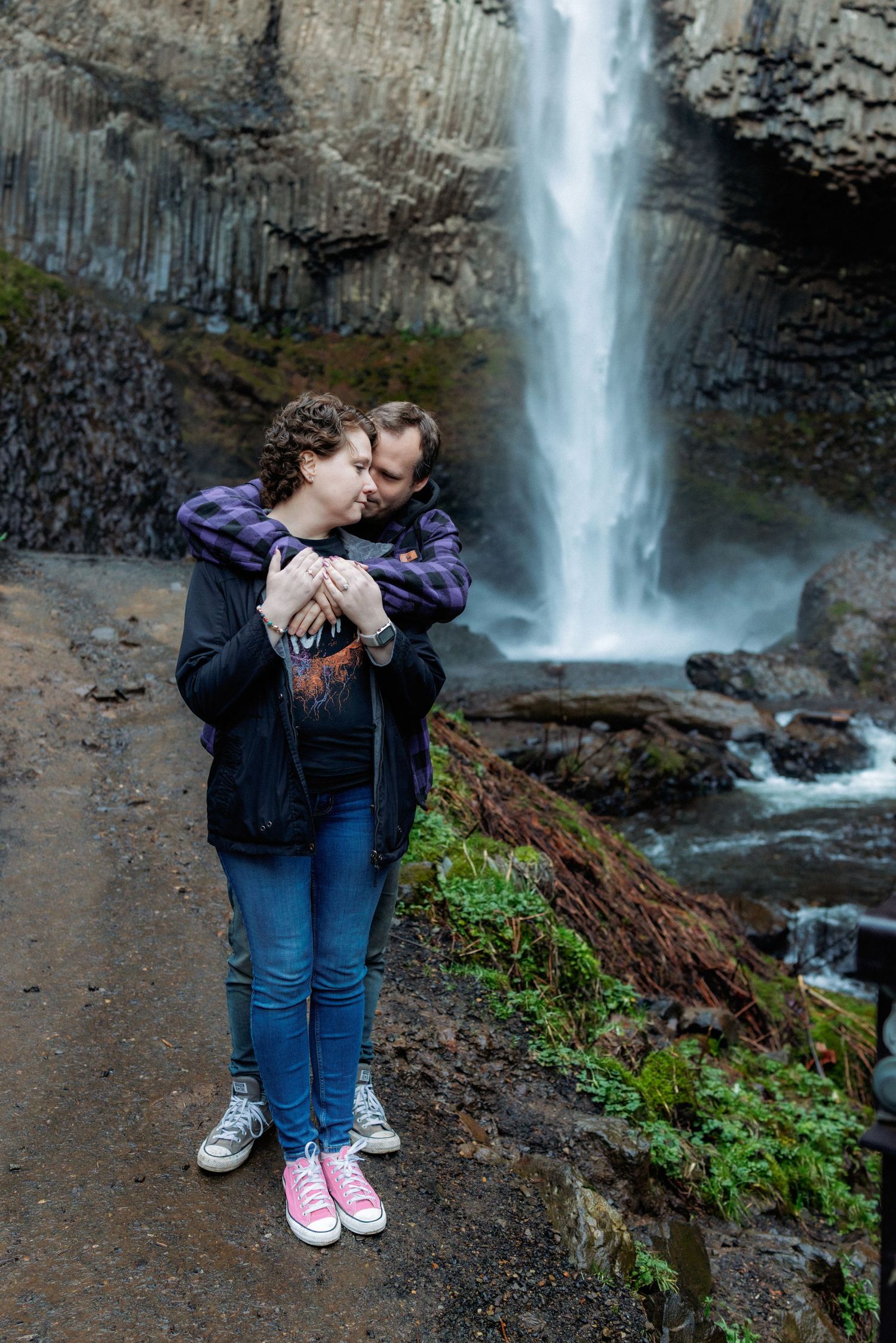 A scenic waterfall cascades down rocky cliffs as visitors admire the natural beauty from a viewing area.