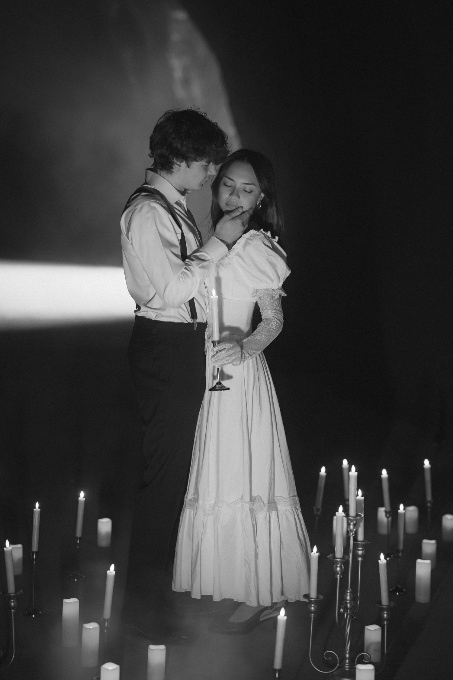 A romantic vintage-style portrait of a couple embracing among lit candles in black and white.