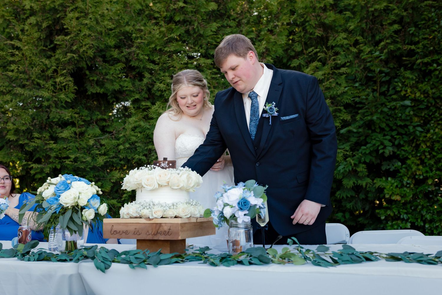 Bride and groom cutting a white wedding cake together at an elegant outdoor reception table.