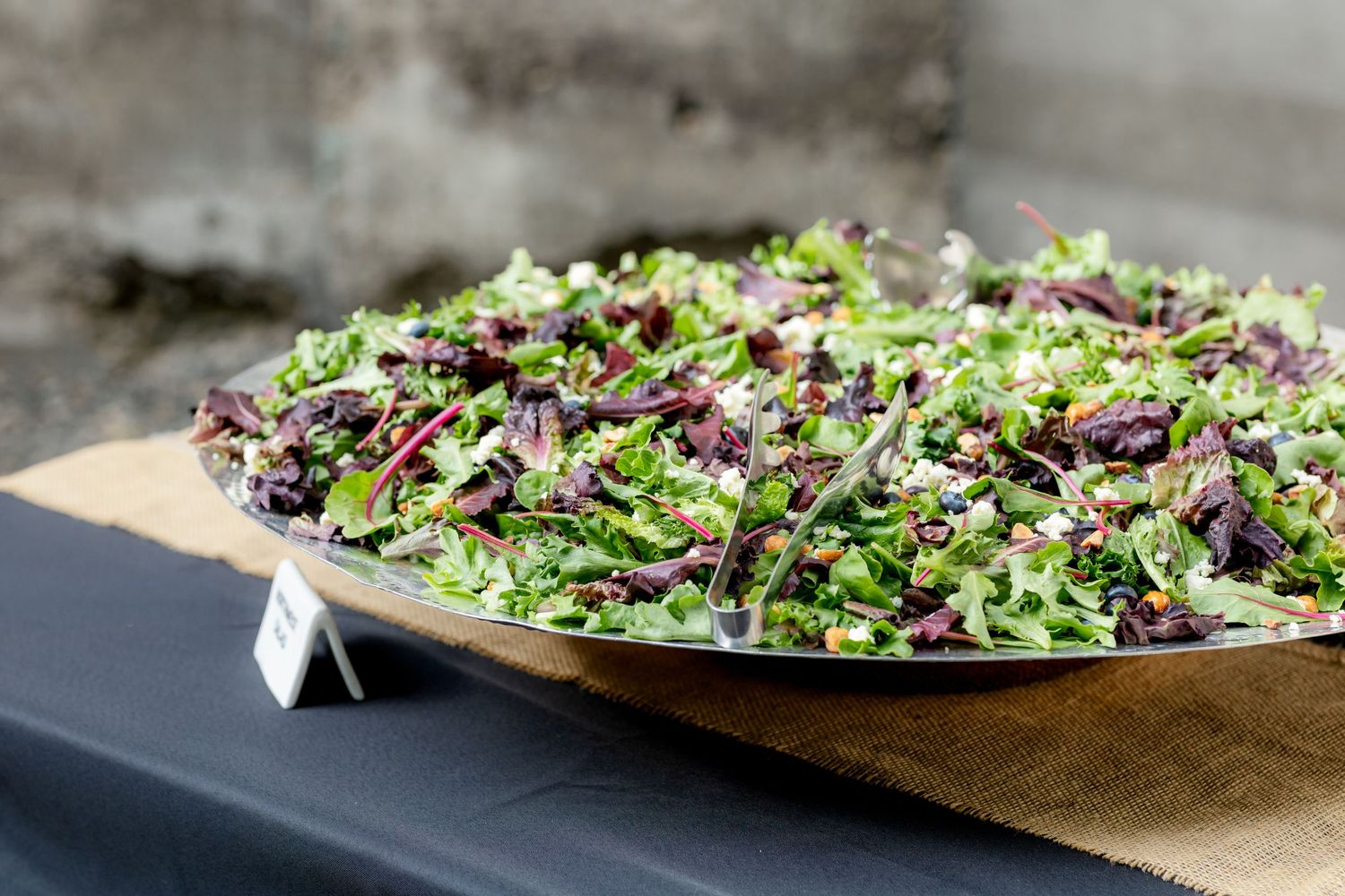 Large wooden bowl filled with fresh mixed green salad at catered event.