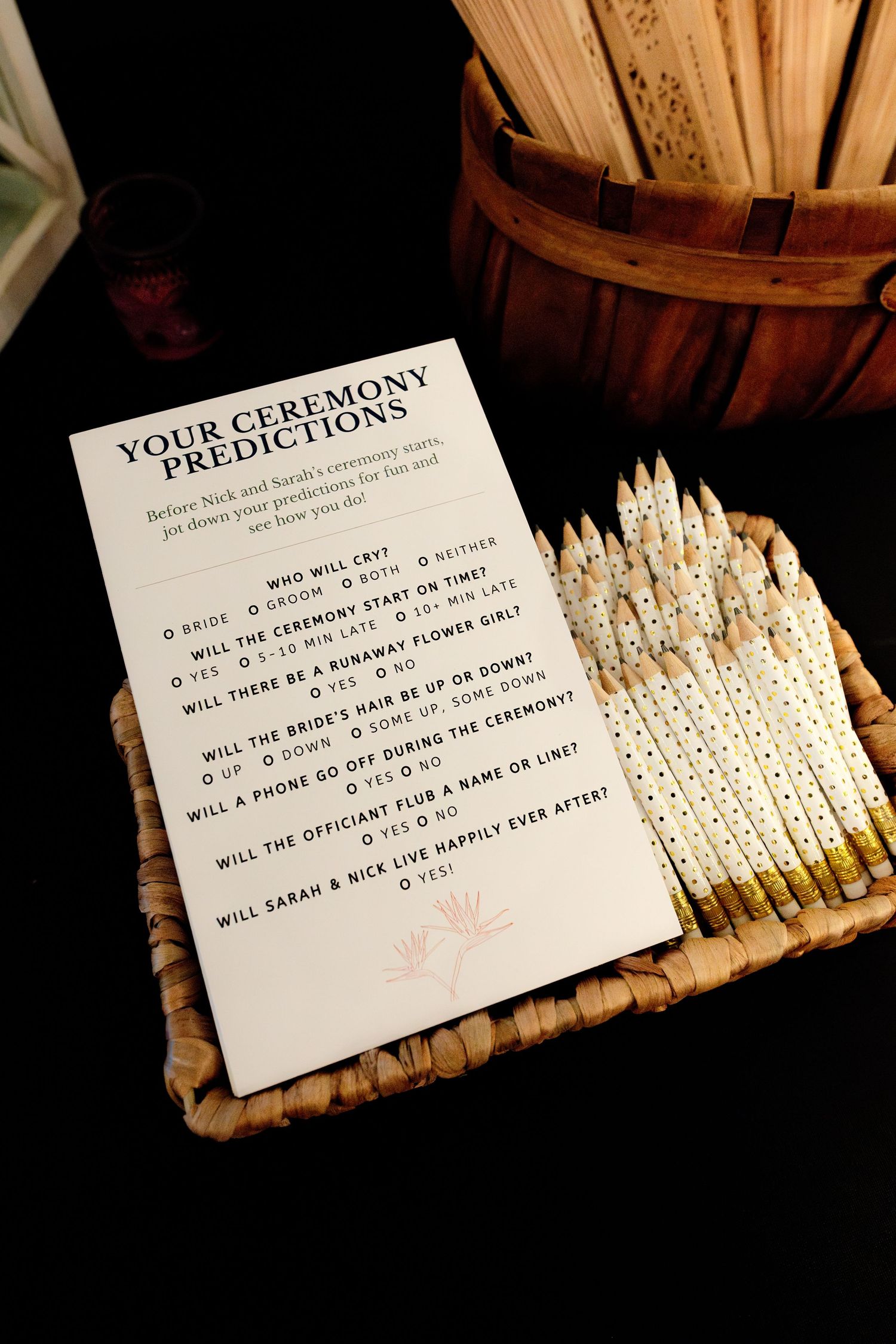 Wedding ceremony prediction game card displayed in a basket with decorative pencils at reception.