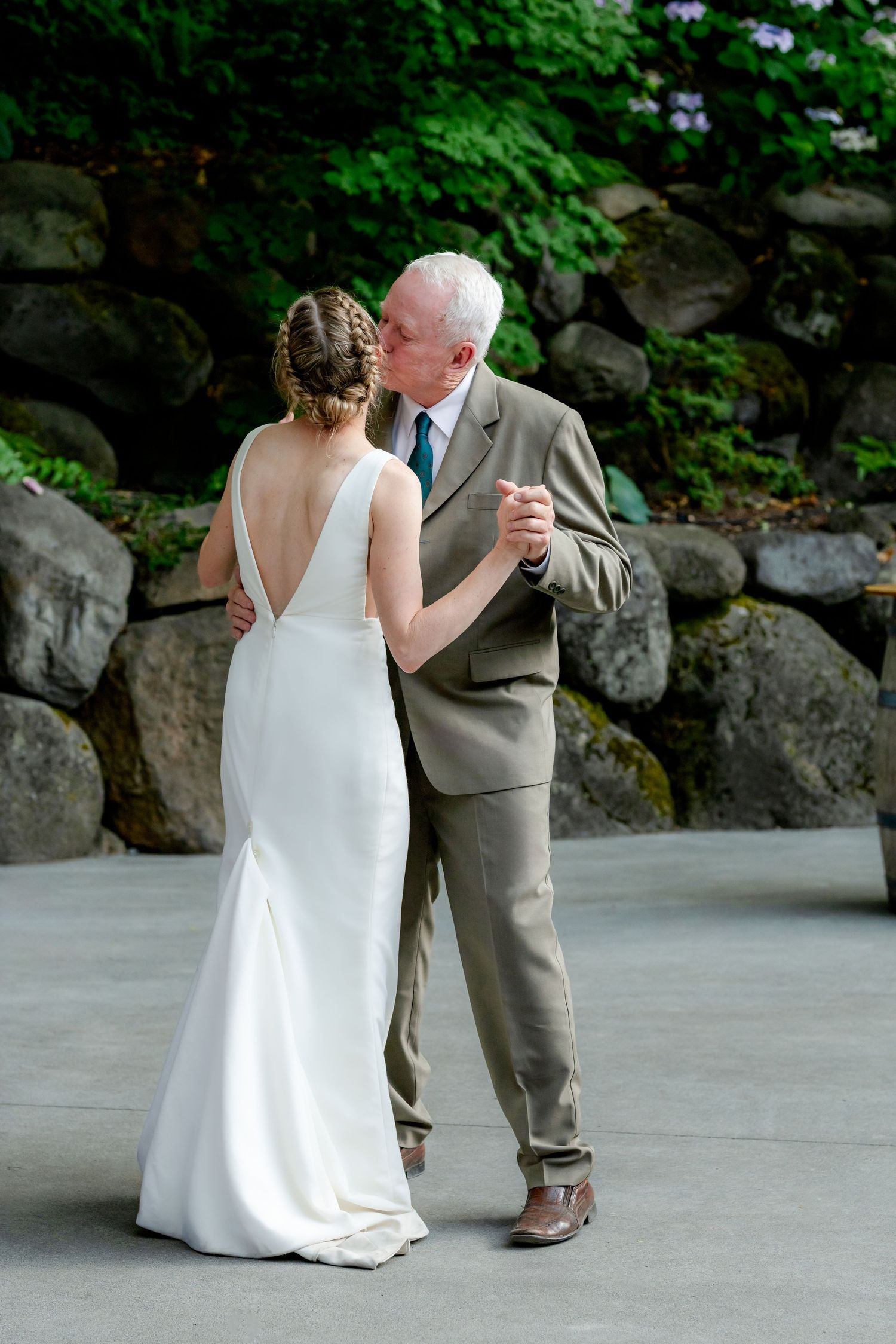 Bride and older man share a tender kiss during father-daughter dance at outdoor wedding reception.