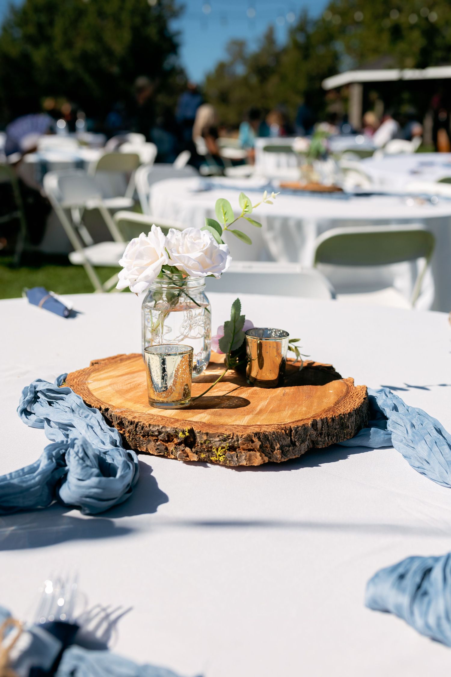 Rustic wedding centerpiece with white roses in mason jar on wood slice with gold candles.
