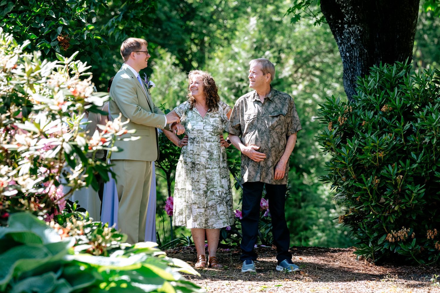 Three guests conversing among lush green garden foliage at an outdoor wedding celebration.