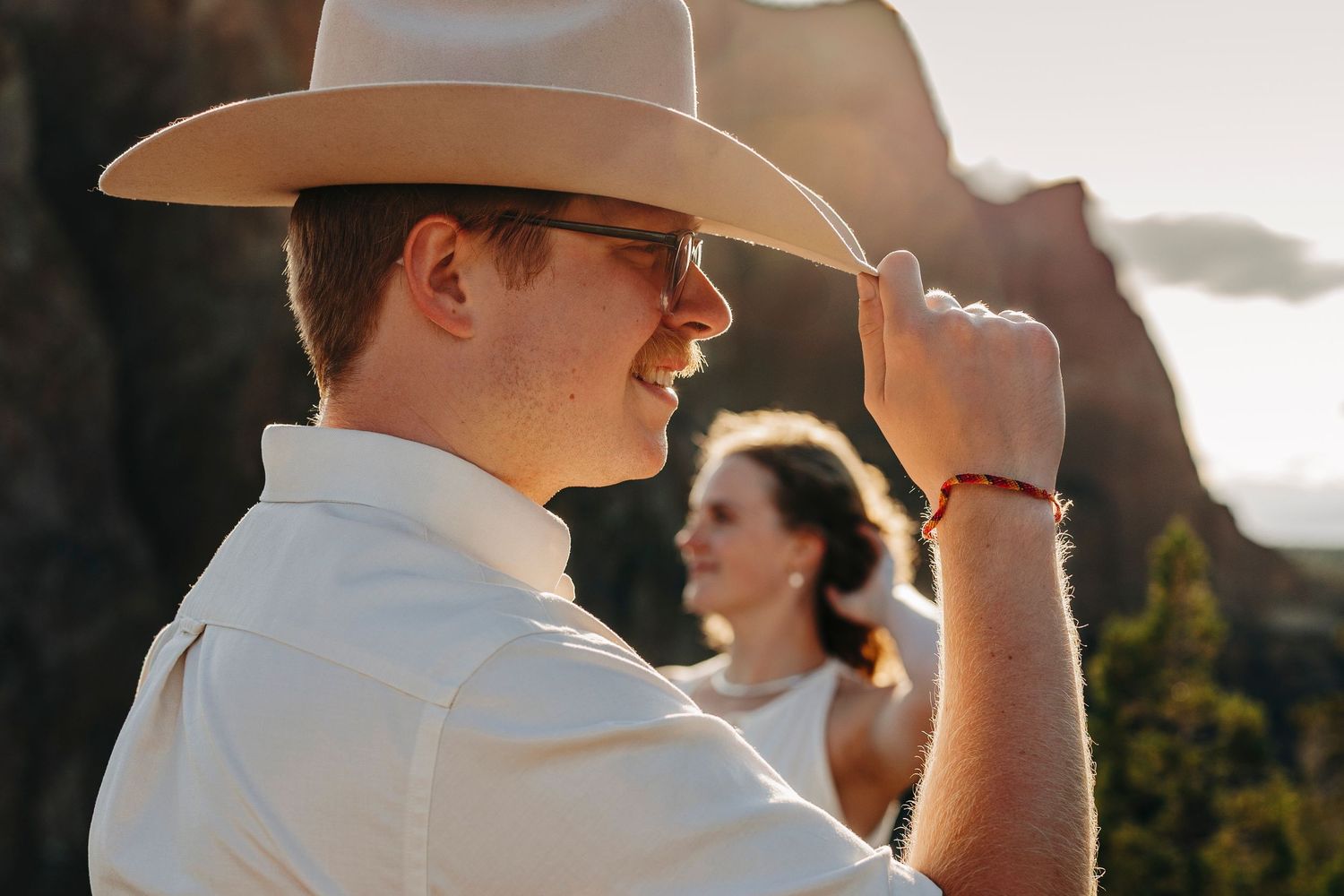 A person in a cowboy hat and white shirt stands in profile against a sunset landscape.