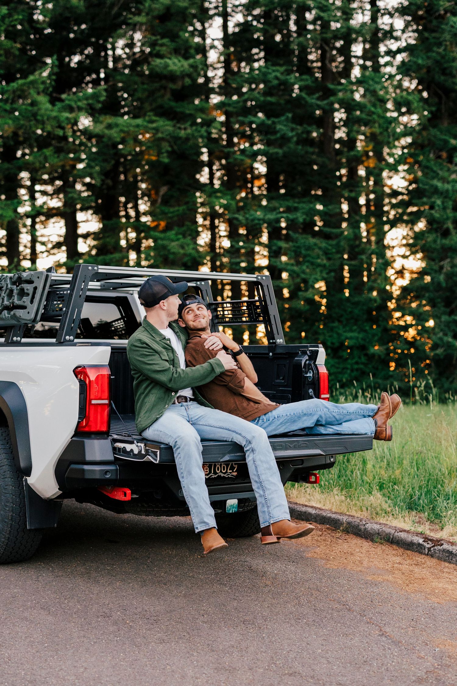 Two people sitting in the back of a pickup truck against a forested backdrop at sunset.