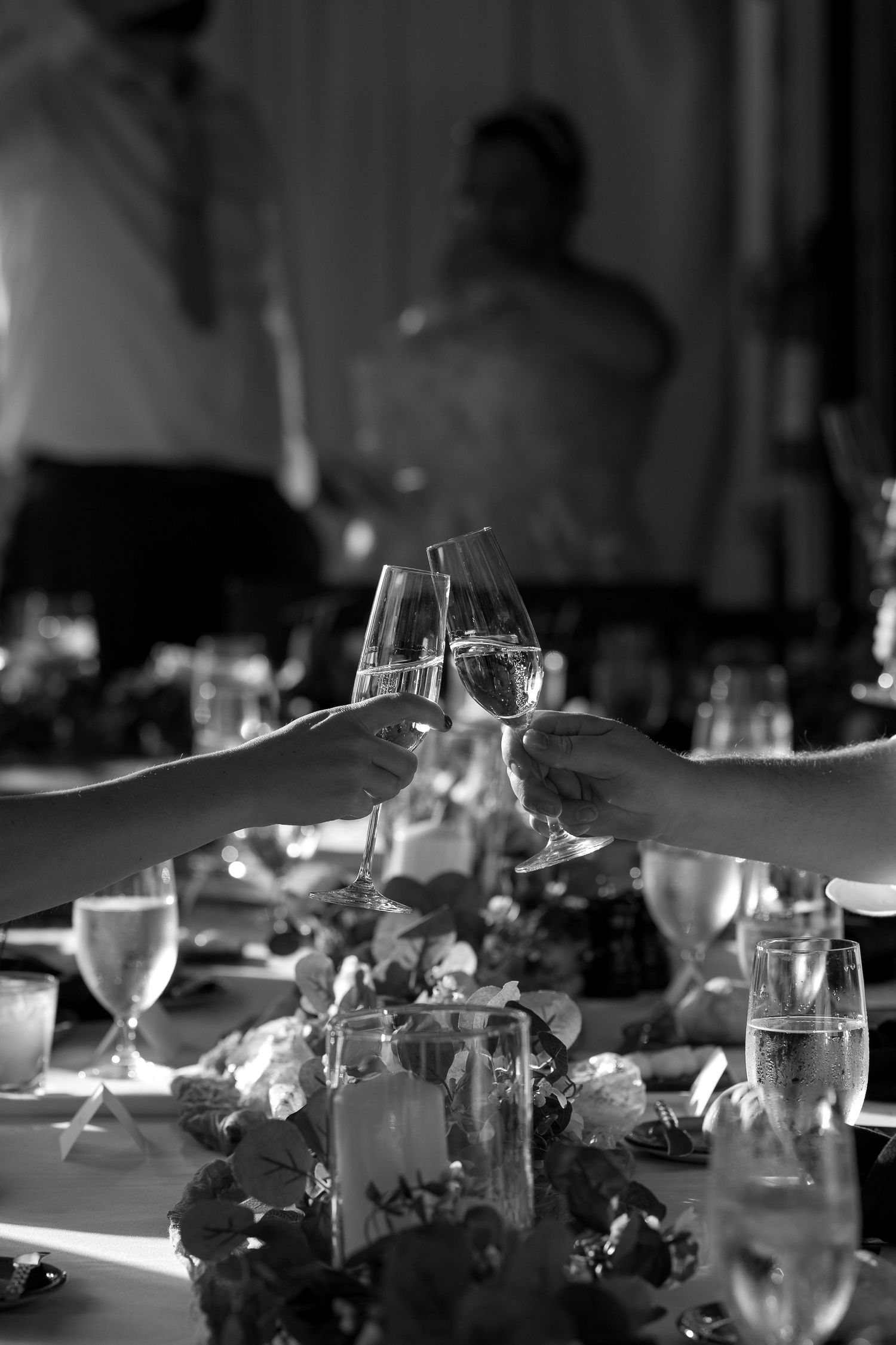 Two hands toasting with champagne glasses at an elegant dinner table setting.