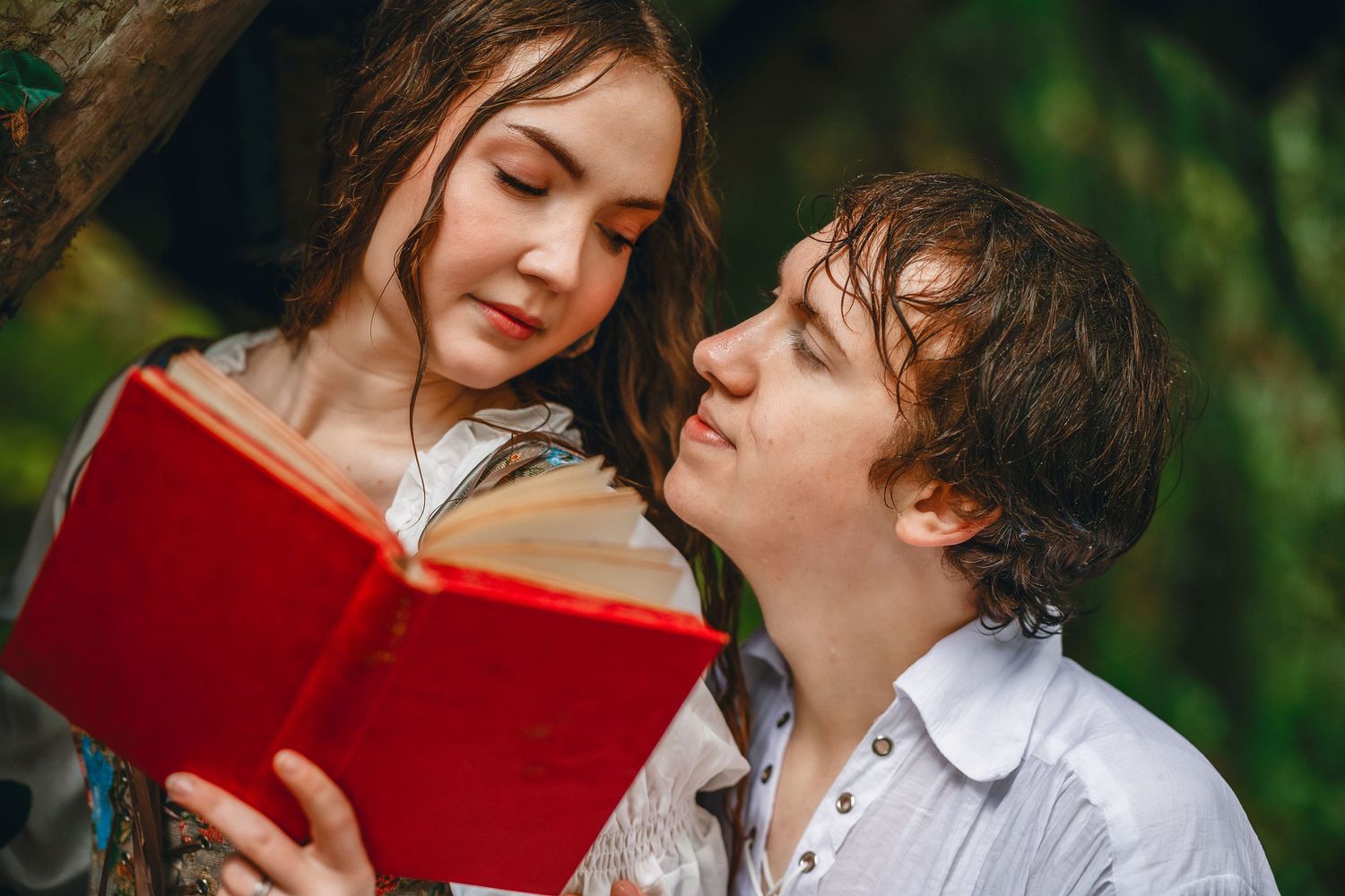 Romantic couple sharing intimate moments while reading a red book together in a garden setting.