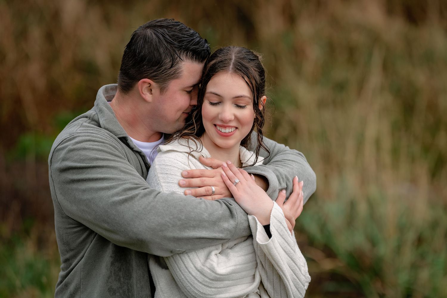 A couple embraces outdoors while sharing a tender moment in a natural setting with tall grass in the background.