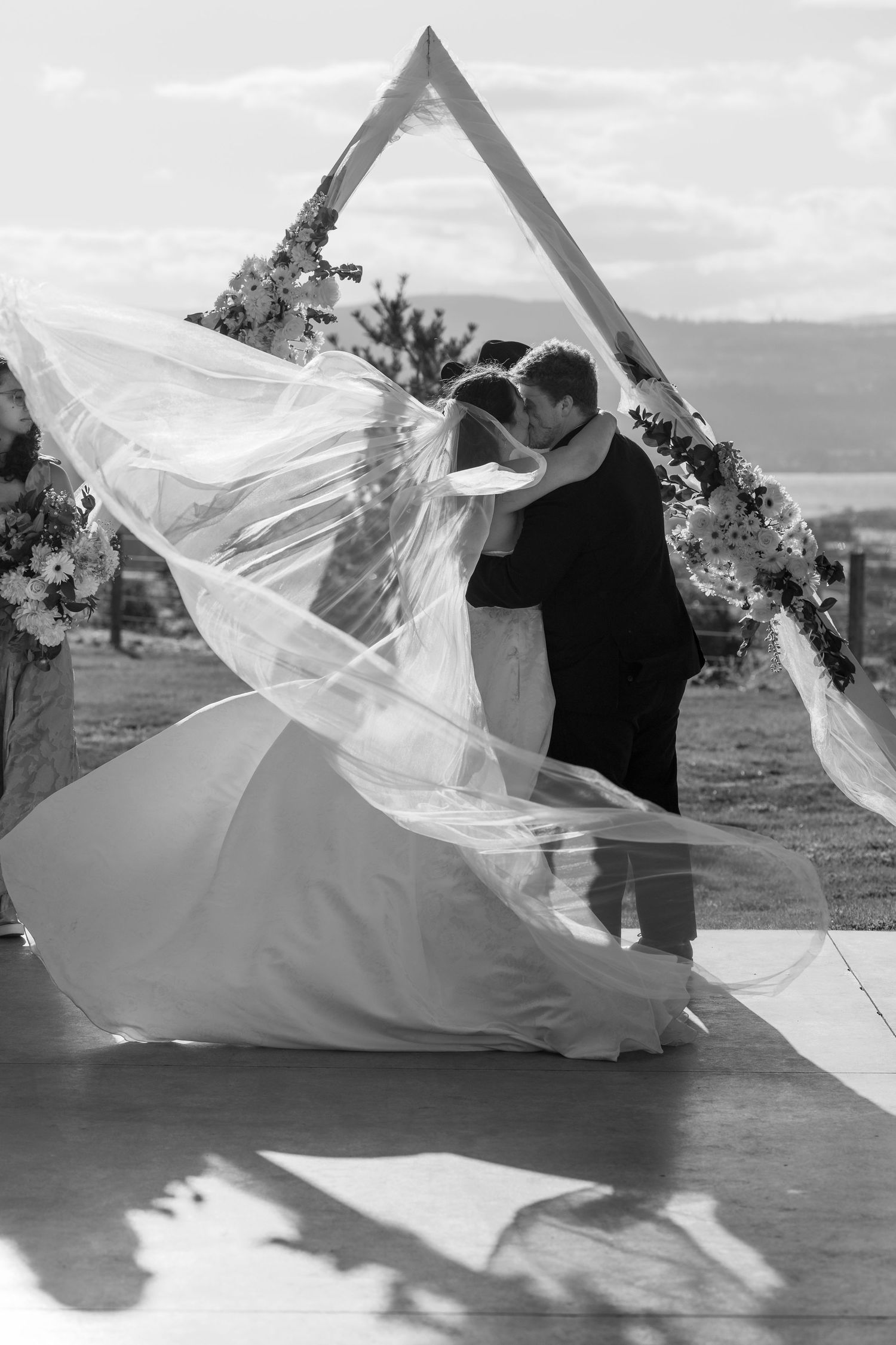 Dramatic black and white photo of bride's veil flowing in the wind during outdoor wedding photoshoot.