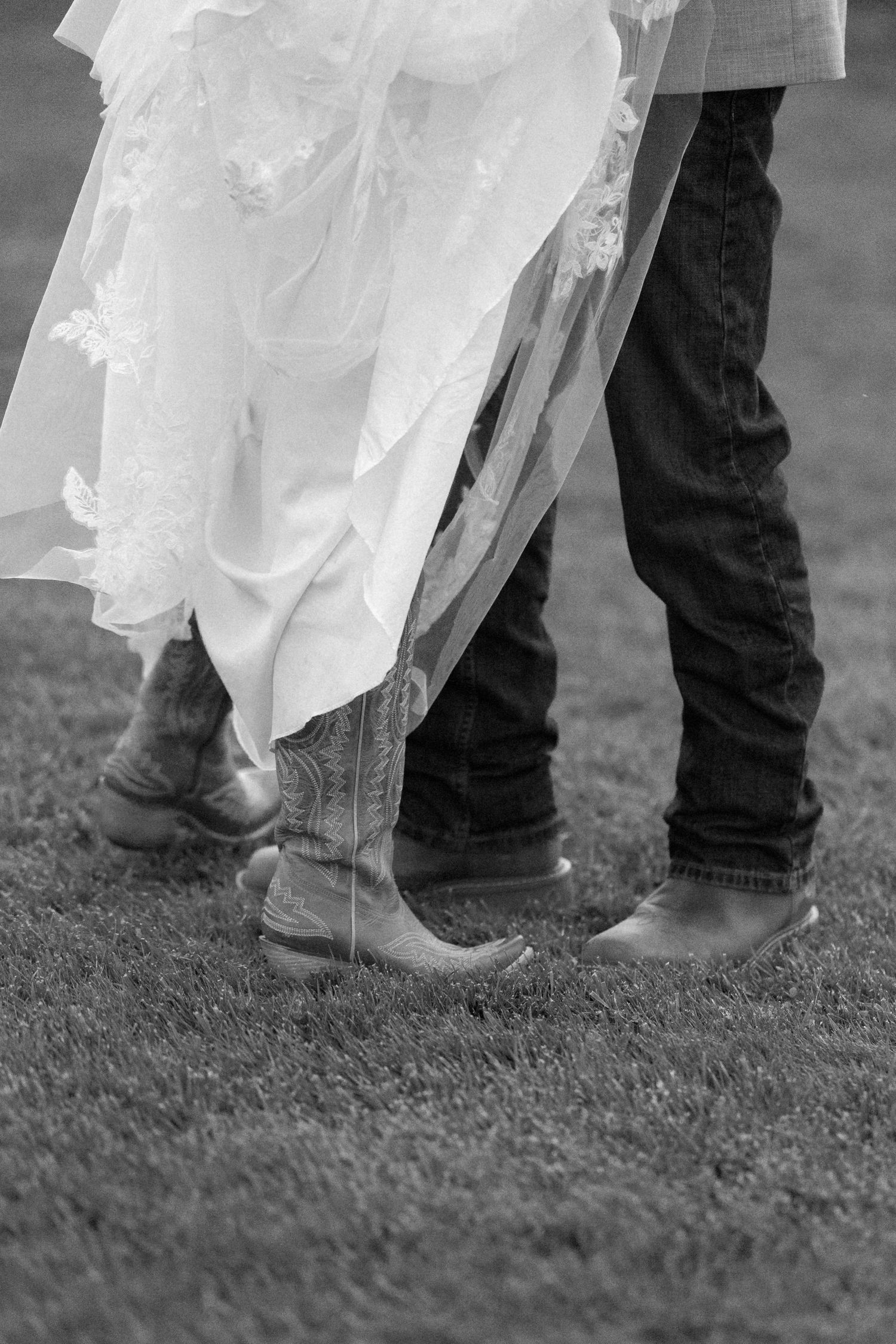 Black and white detail shot of wedding attire and boots on grass.