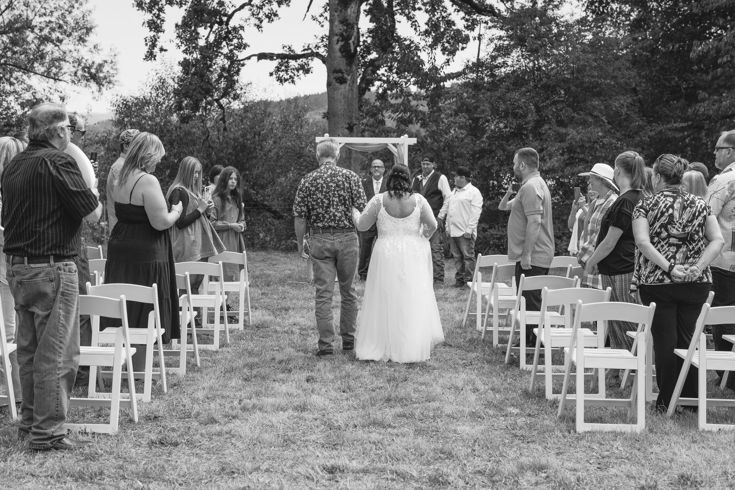 Outdoor wedding ceremony setup with white chairs and guests in attendance.
