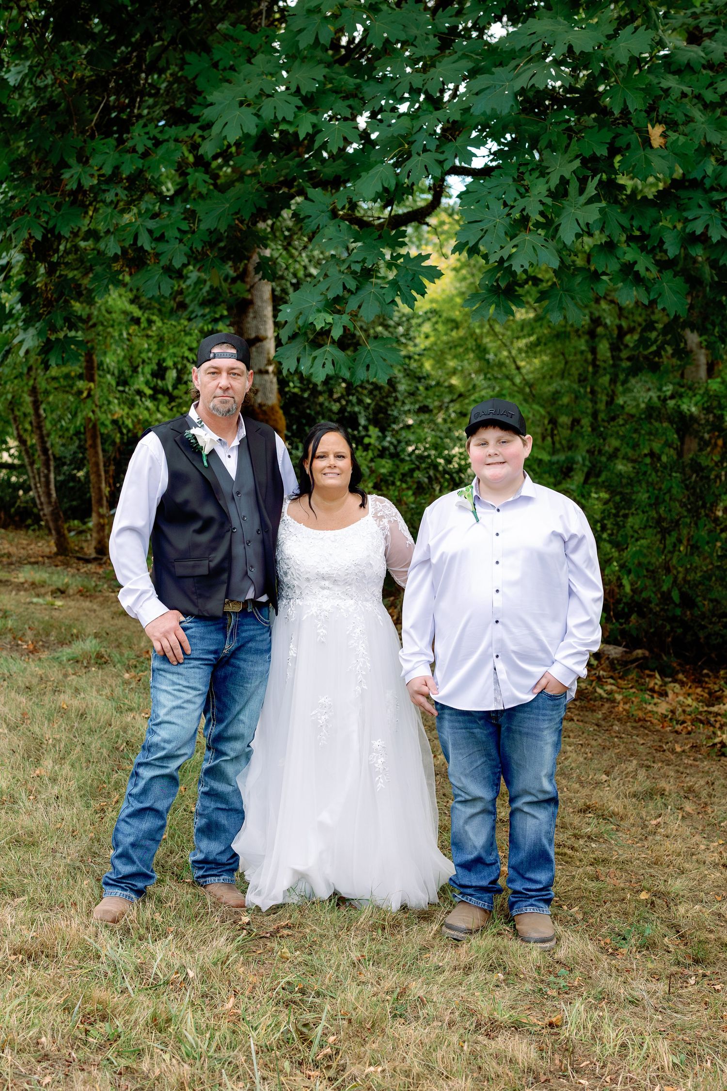 A group poses for outdoor portraits on a grassy hillside with green trees in the background.