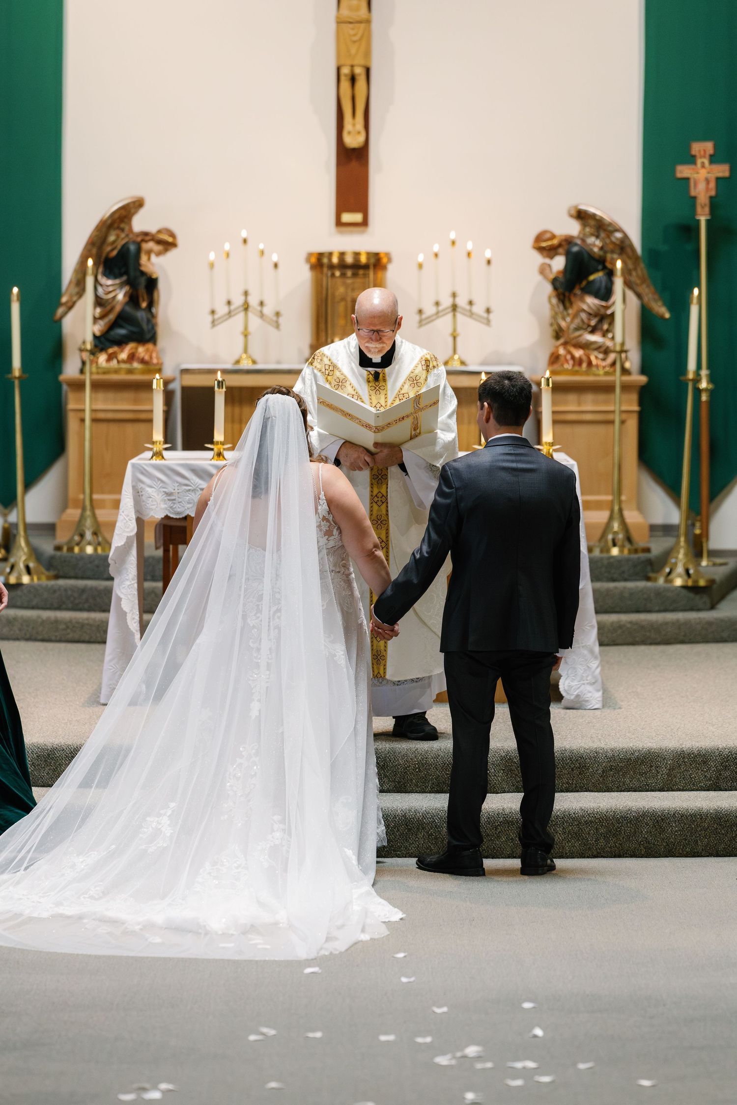 Wedding ceremony in a church with flowing white bridal veil and green altar decorations.
