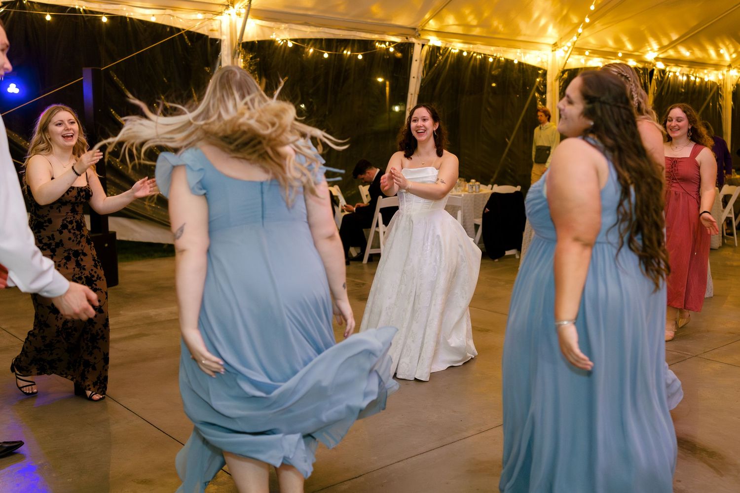 Wedding guests in light blue bridesmaid dresses dancing and celebrating on the dance floor.