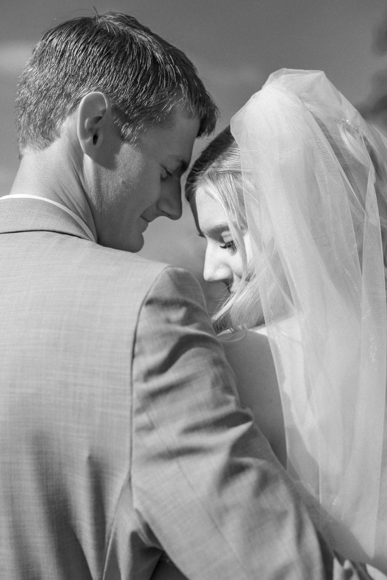 Intimate black and white portrait of newlyweds sharing tender moment with bridal veil.