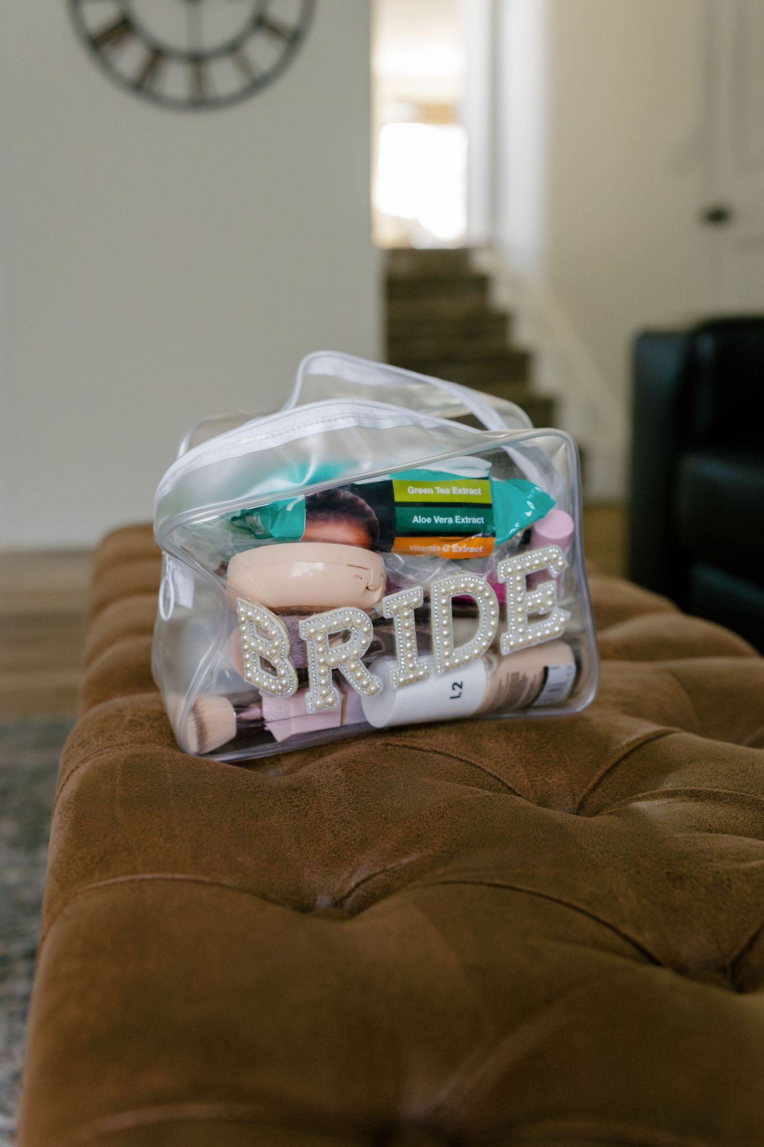 A clear bag containing 'BRIDE' text and wedding day essentials sits on a brown velvet surface.