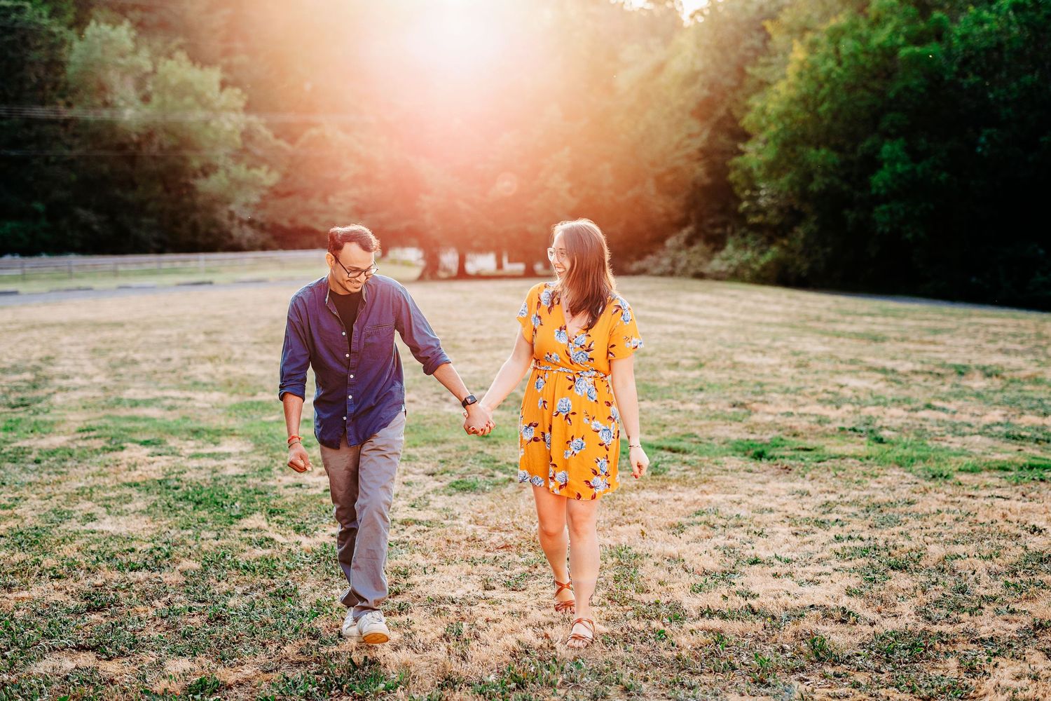 Couple walking through a sun-drenched field during golden hour.