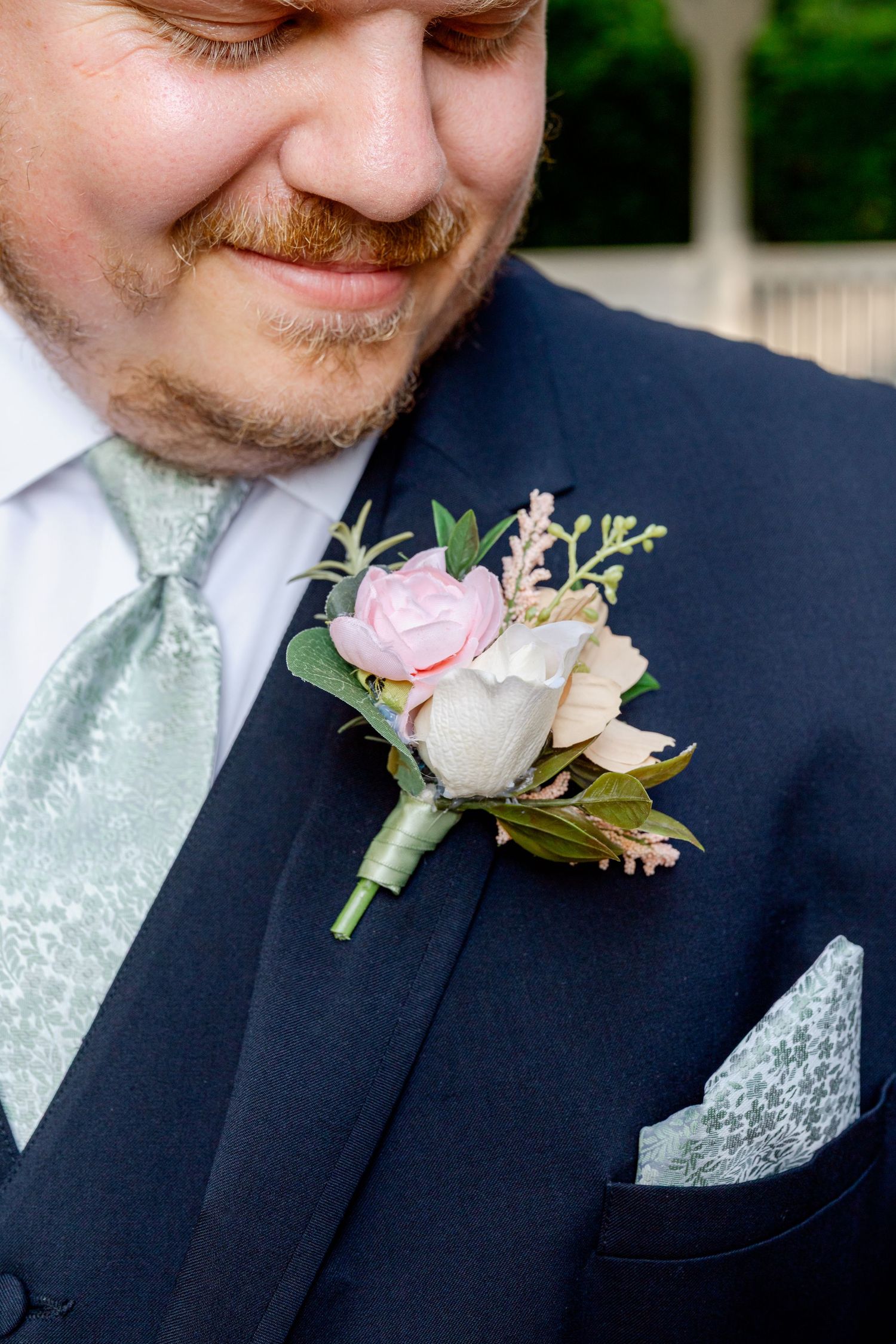 Close-up of pink and white rose boutonniere on groom's navy suit with sage green tie.