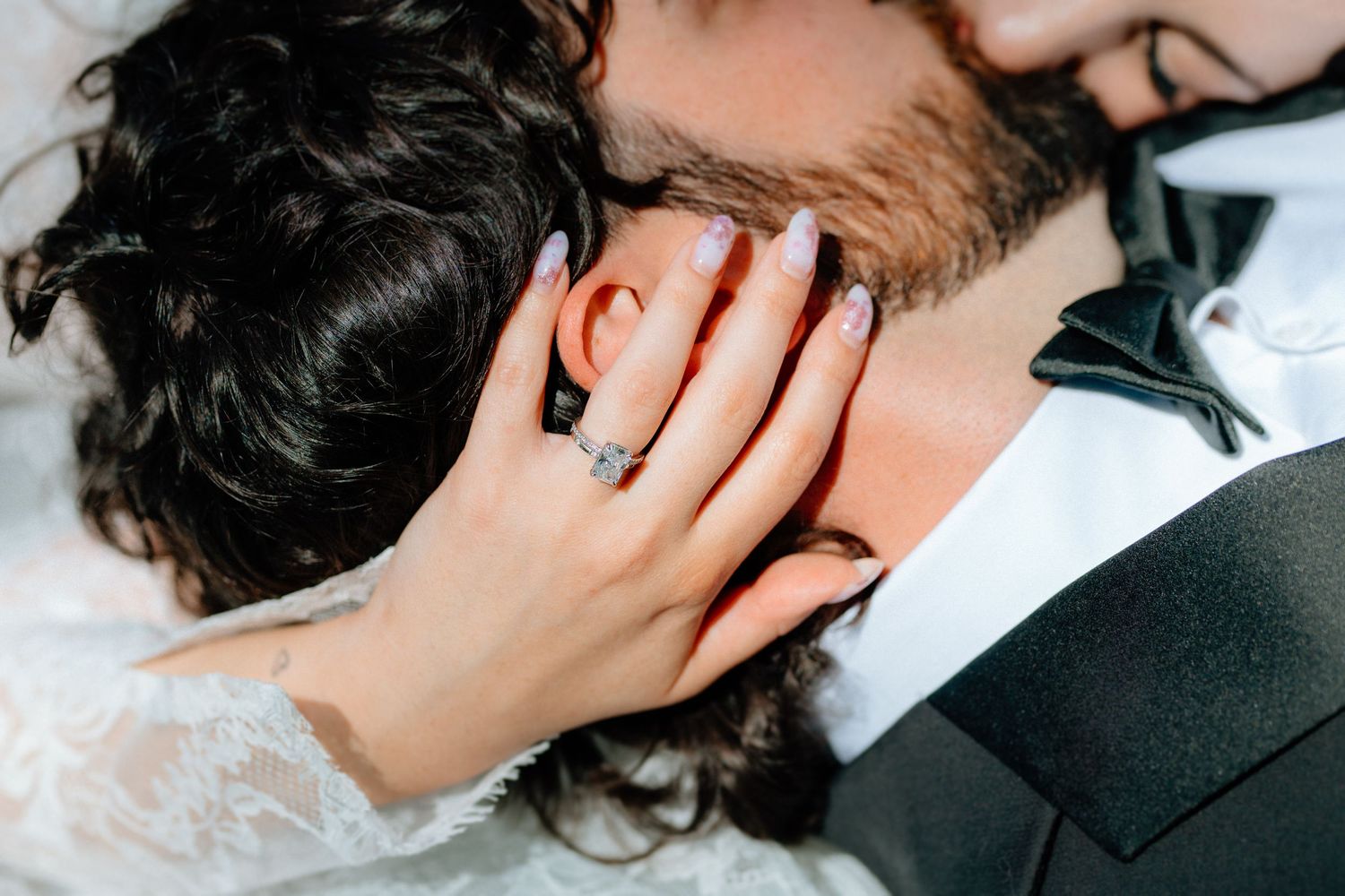Close-up of bride and groom embracing, showcasing elegant diamond engagement ring with purple manicure on wedding day.