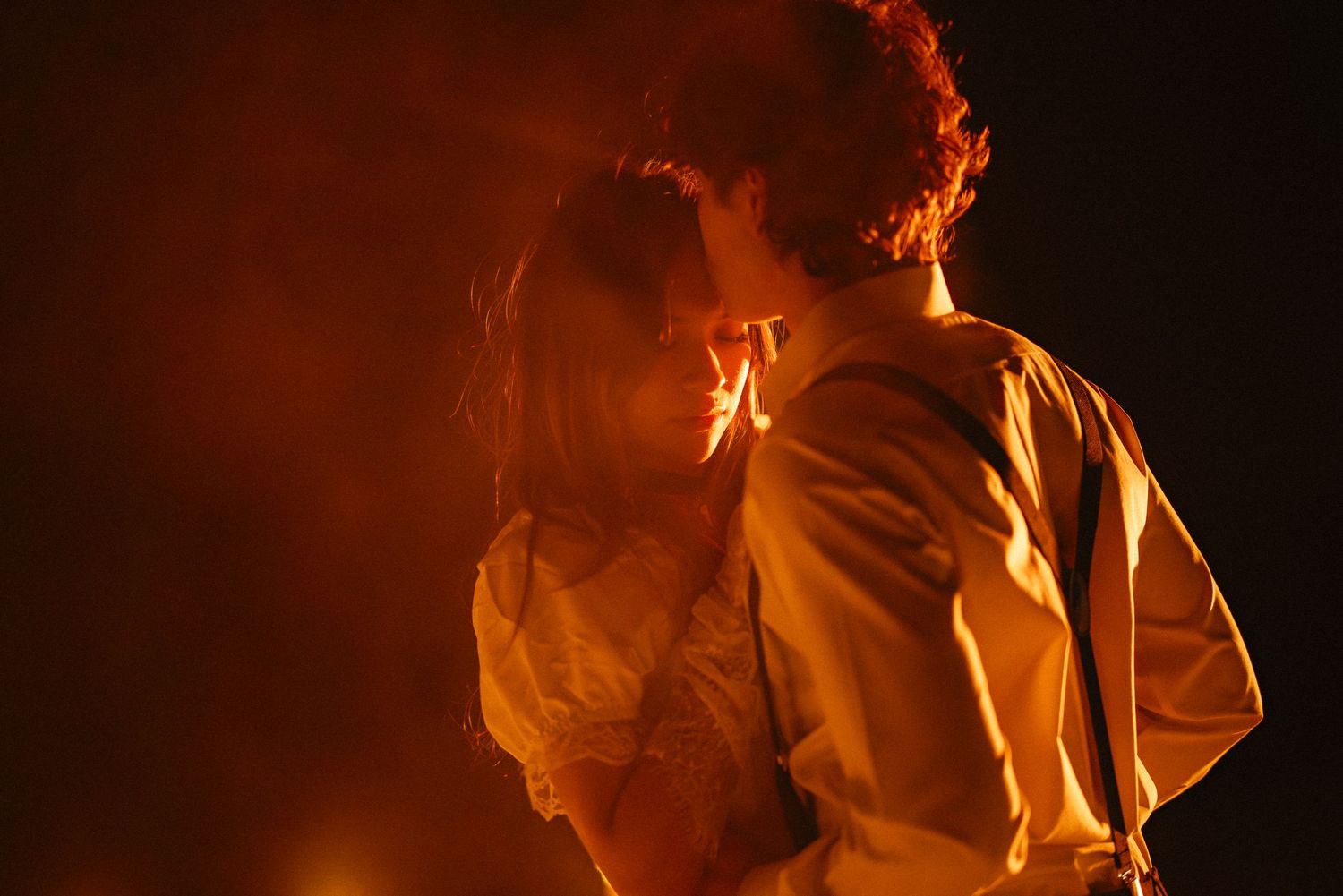 Romantic couple embracing in dramatic orange-red smoky light against dark background.