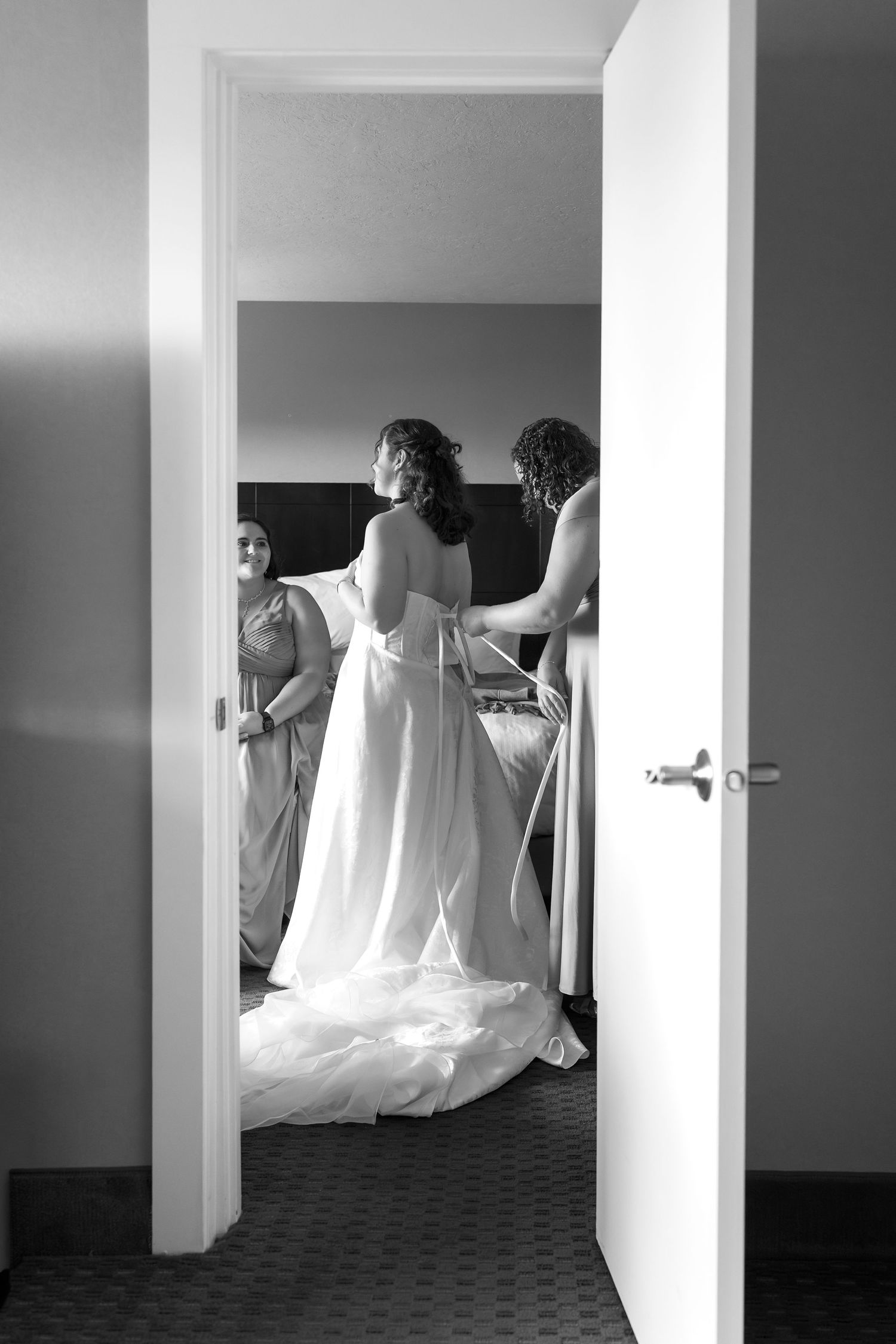Black and white sequence shows wedding dress preparation in hotel hallway.