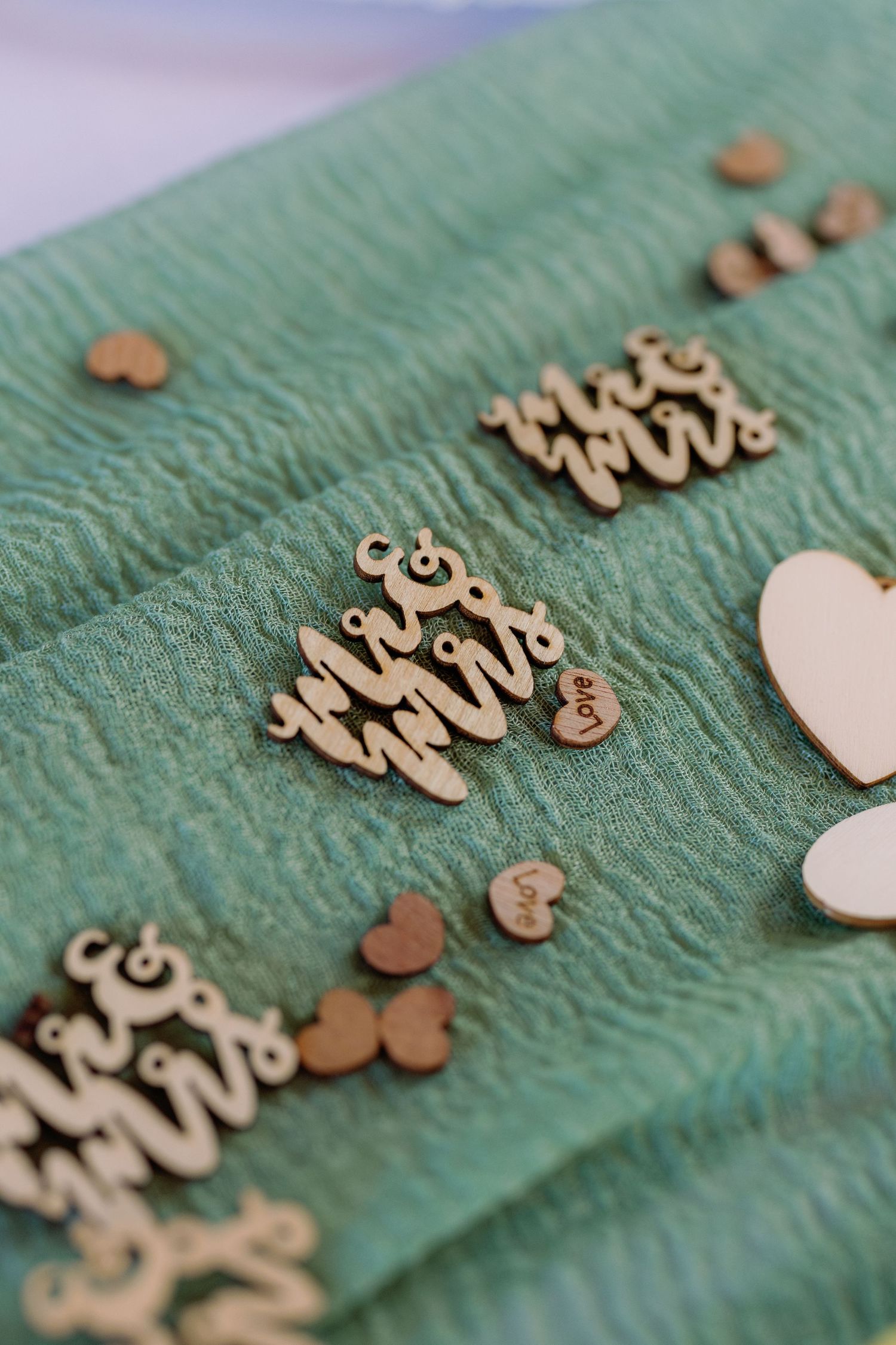 Wooden decorative letters and hearts arranged on a teal textured surface in a crafting layout.