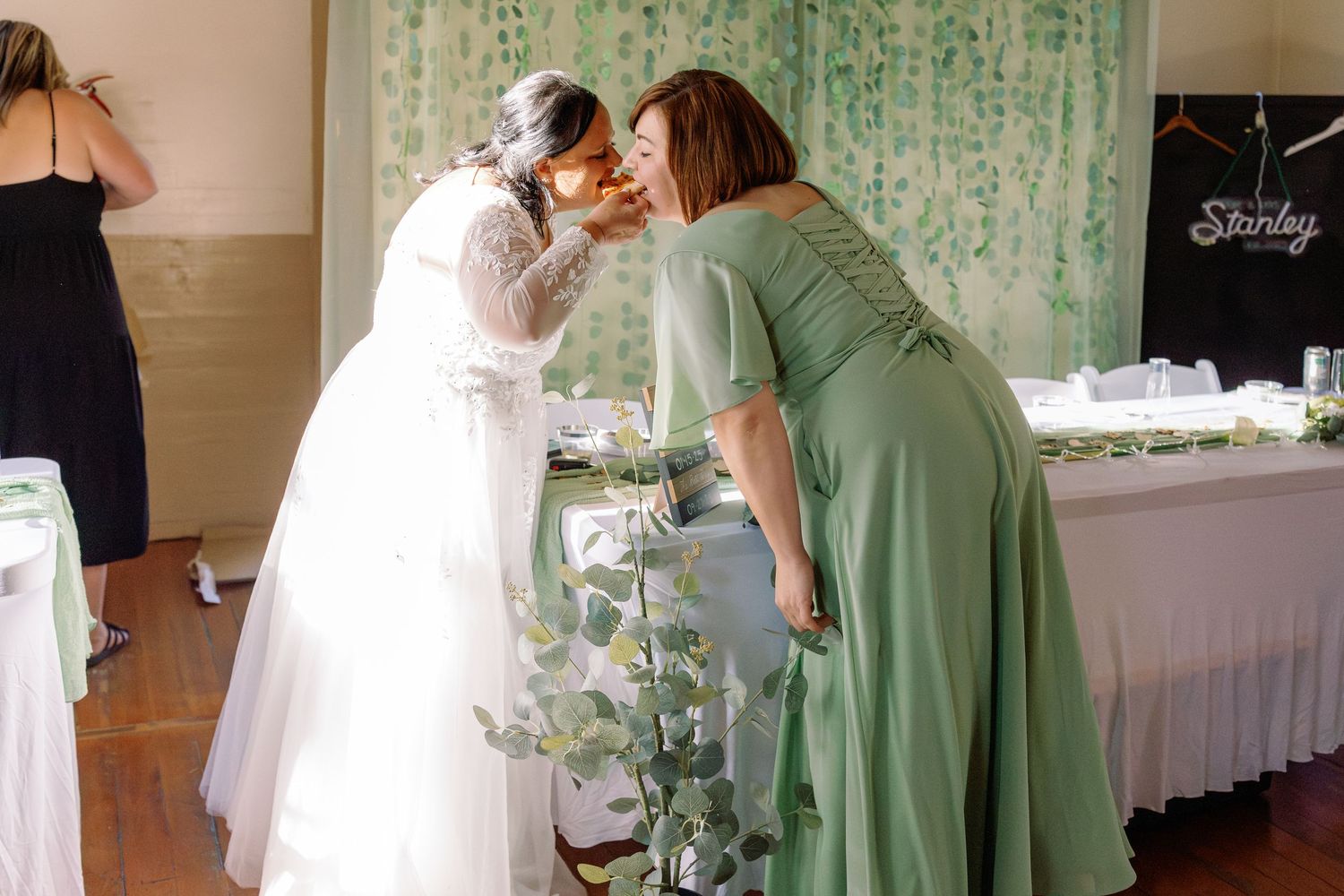 Bridesmaids in sage green dresses help prepare for a wedding ceremony in an elegant white-decorated venue.
