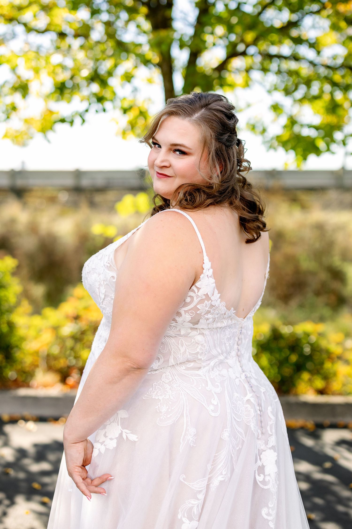 A person in a flowing white lace dress poses outdoors against a backdrop of autumn foliage.
