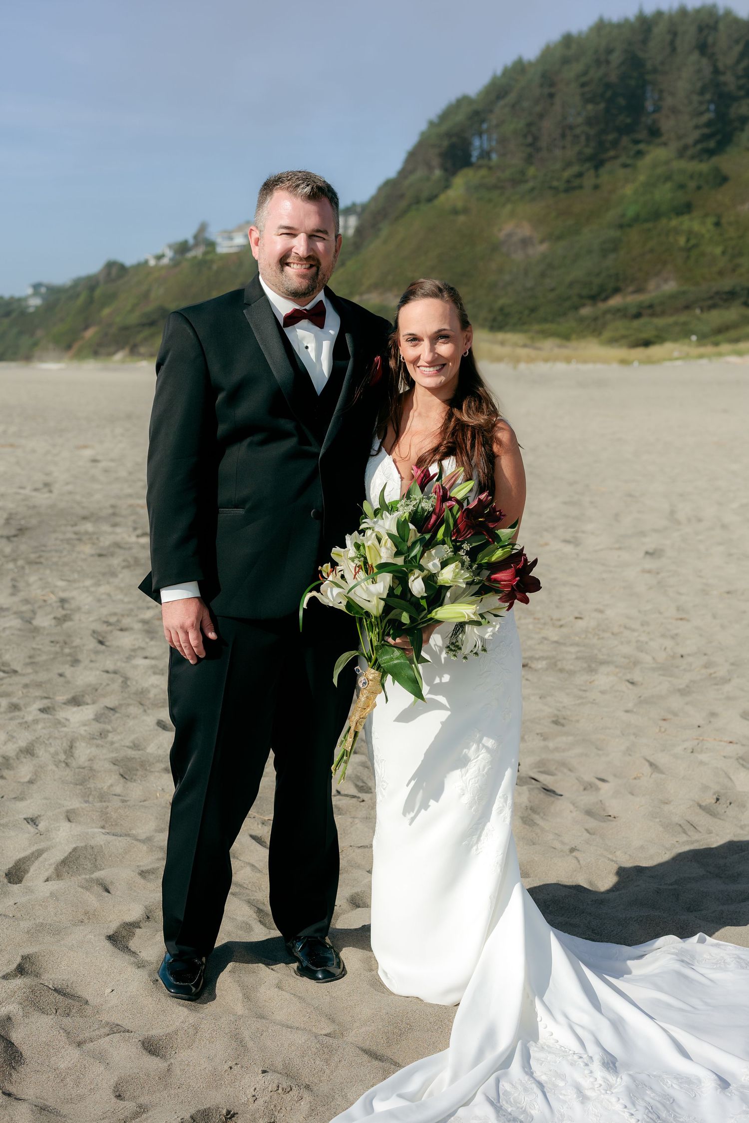 Wedding couple poses for portraits on a scenic beach with coastal cliffs in background.