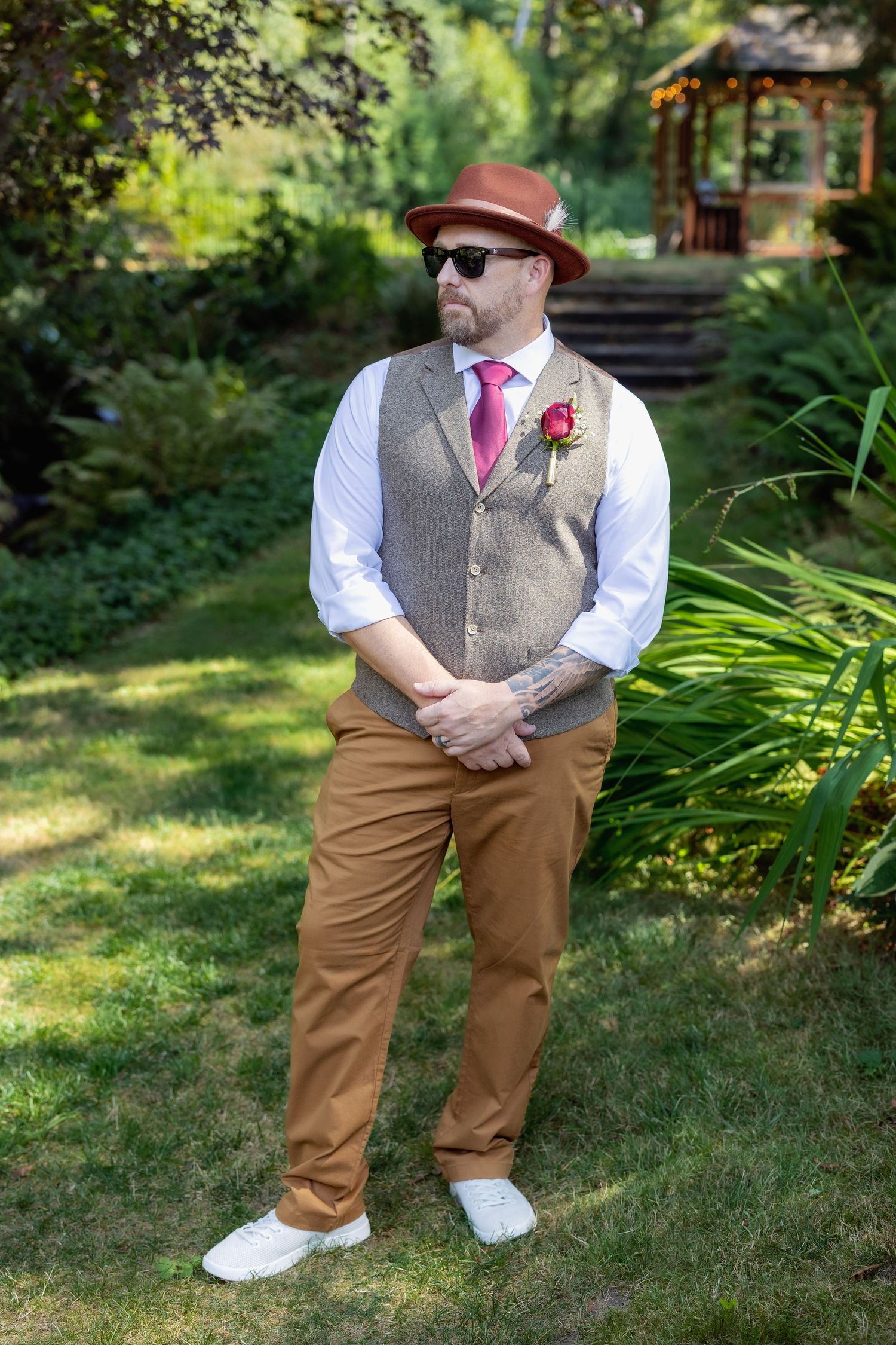 Wedding party member in brown pants and gray vest poses in garden setting.