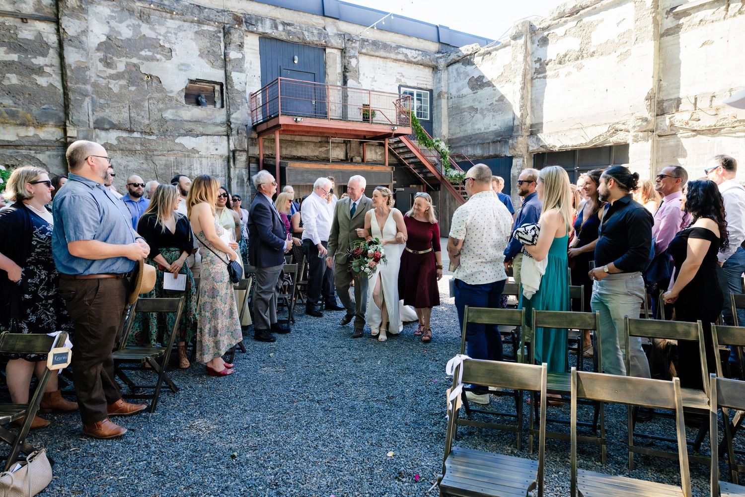 Outdoor wedding ceremony in rustic courtyard with guests gathered around couple amid weathered brick walls.