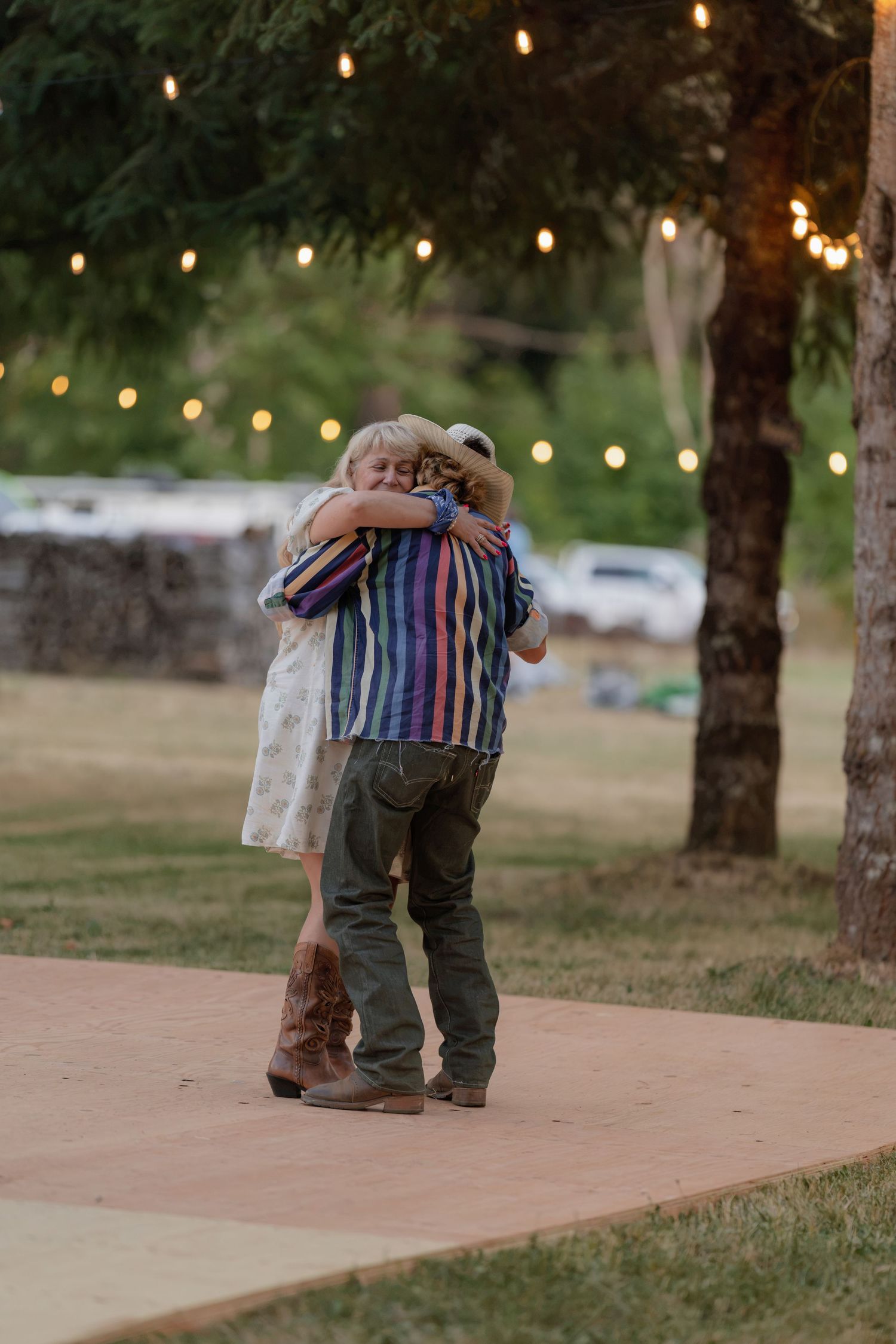 Two children share a sweet hug on an outdoor dance floor with string lights at a rustic wedding.