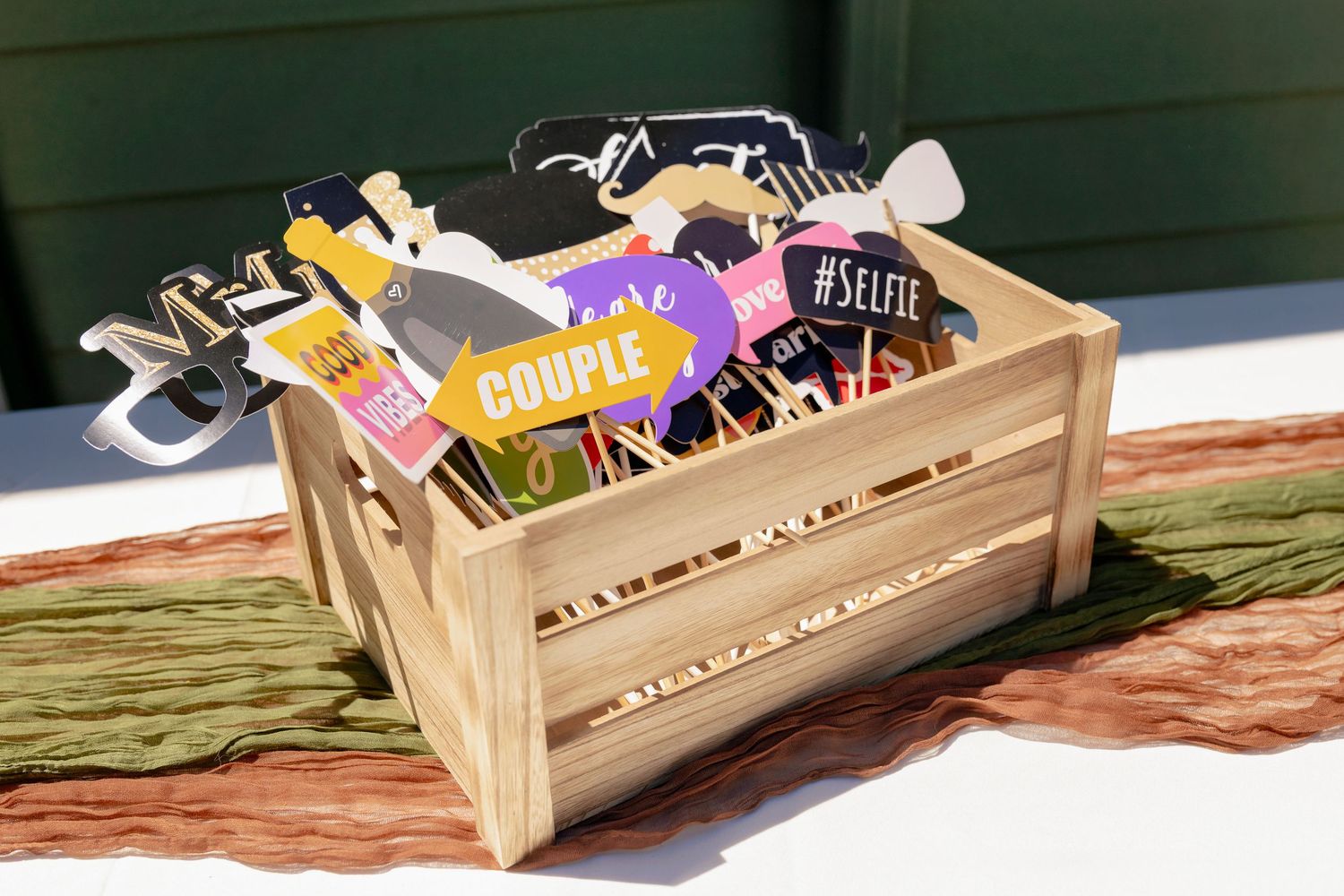 Wooden crate filled with colorful wedding photo booth props including glasses and couple signs.