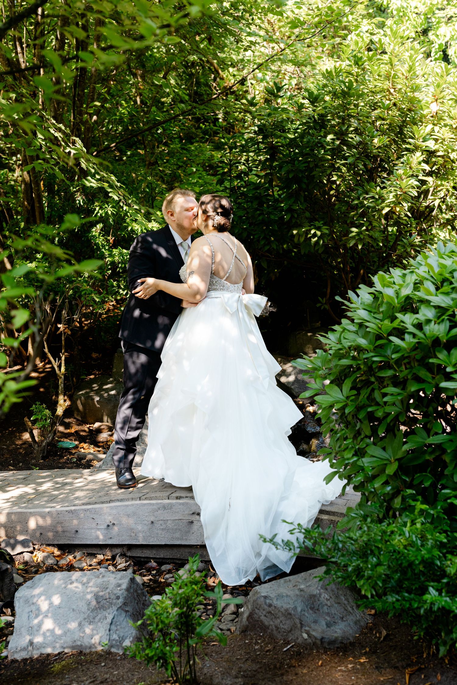 Bride and groom share a romantic kiss surrounded by lush greenery on their wedding day.