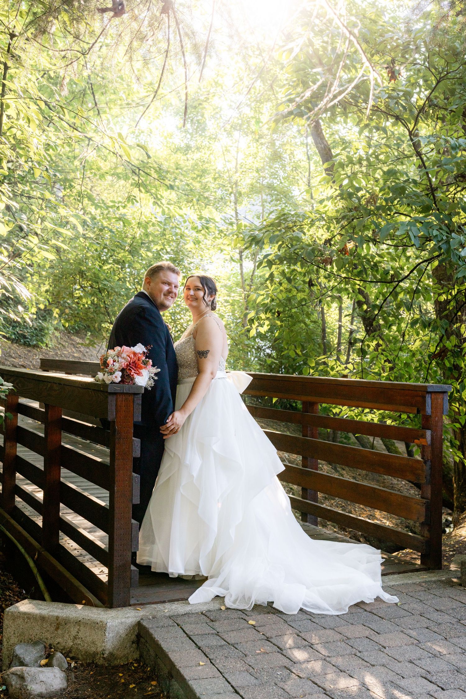 Bride and groom share a romantic moment on a wooden bridge surrounded by lush green trees on their wedding day.