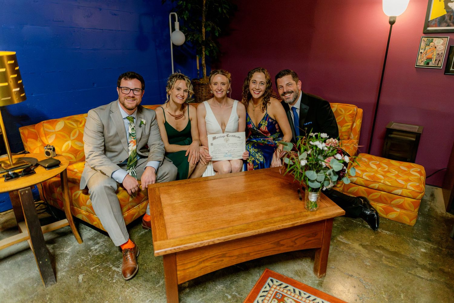 Five people smiling on vintage sofa at wedding.