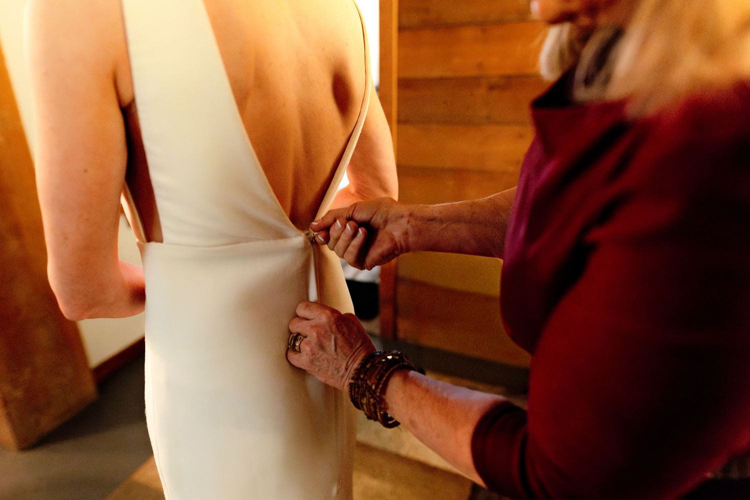 Mother helps bride button the back of her elegant white wedding gown before the ceremony.